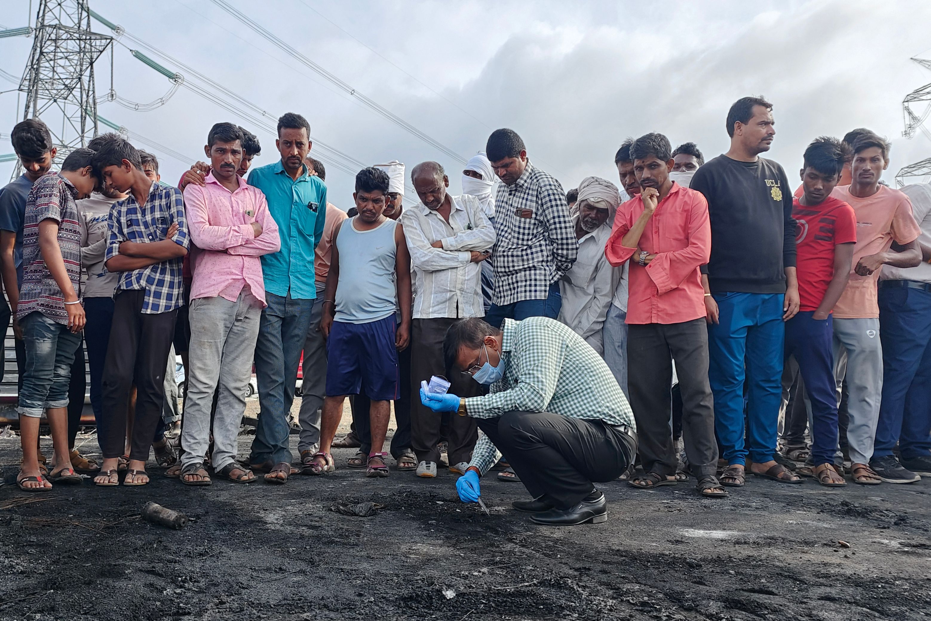 Onlookers stand next to an official collecting samples from the remains of a bus that caught fire along the Samruddhi Expressway