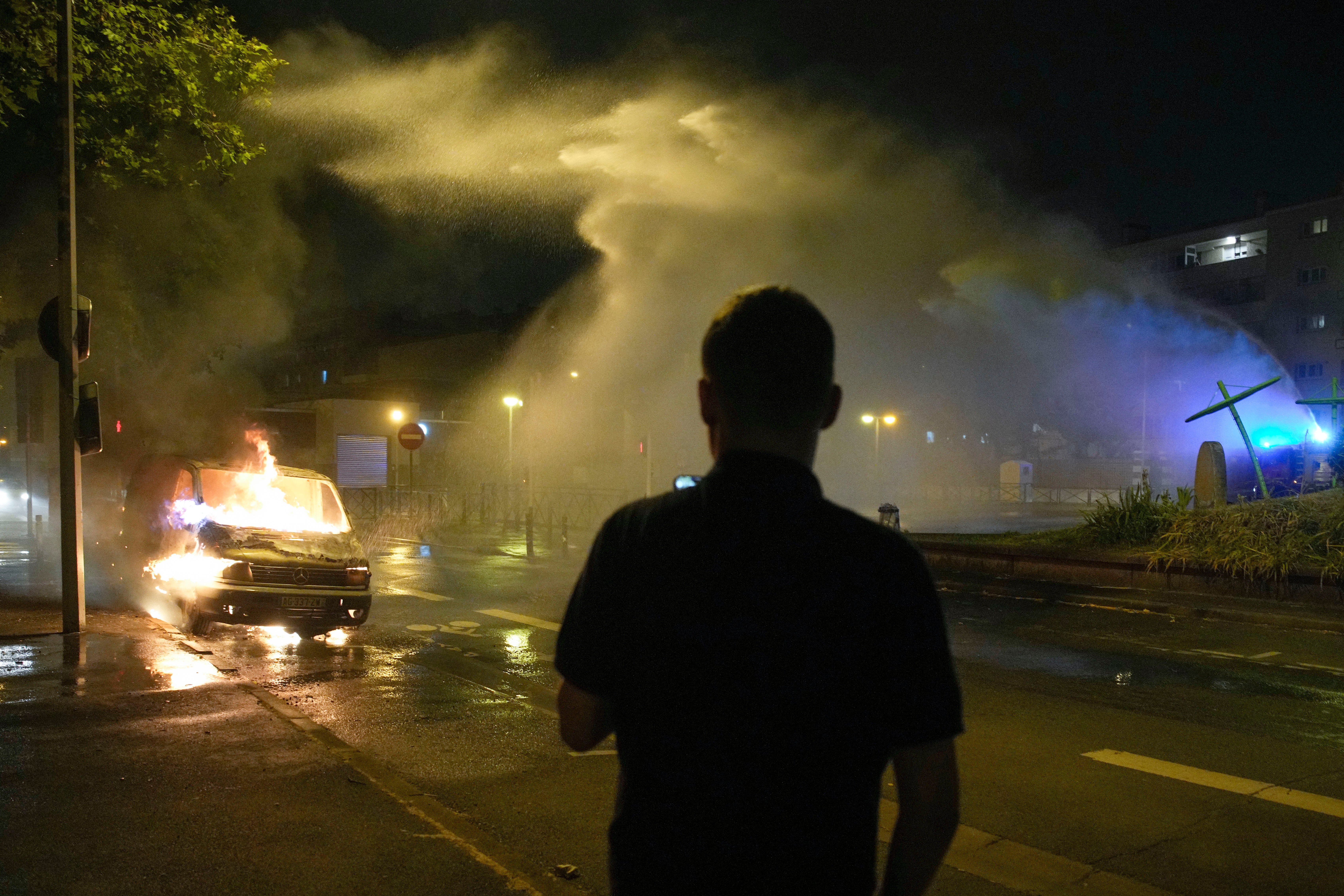 Firefighters use a water hose on a burnt car in Nanterre, outside Paris