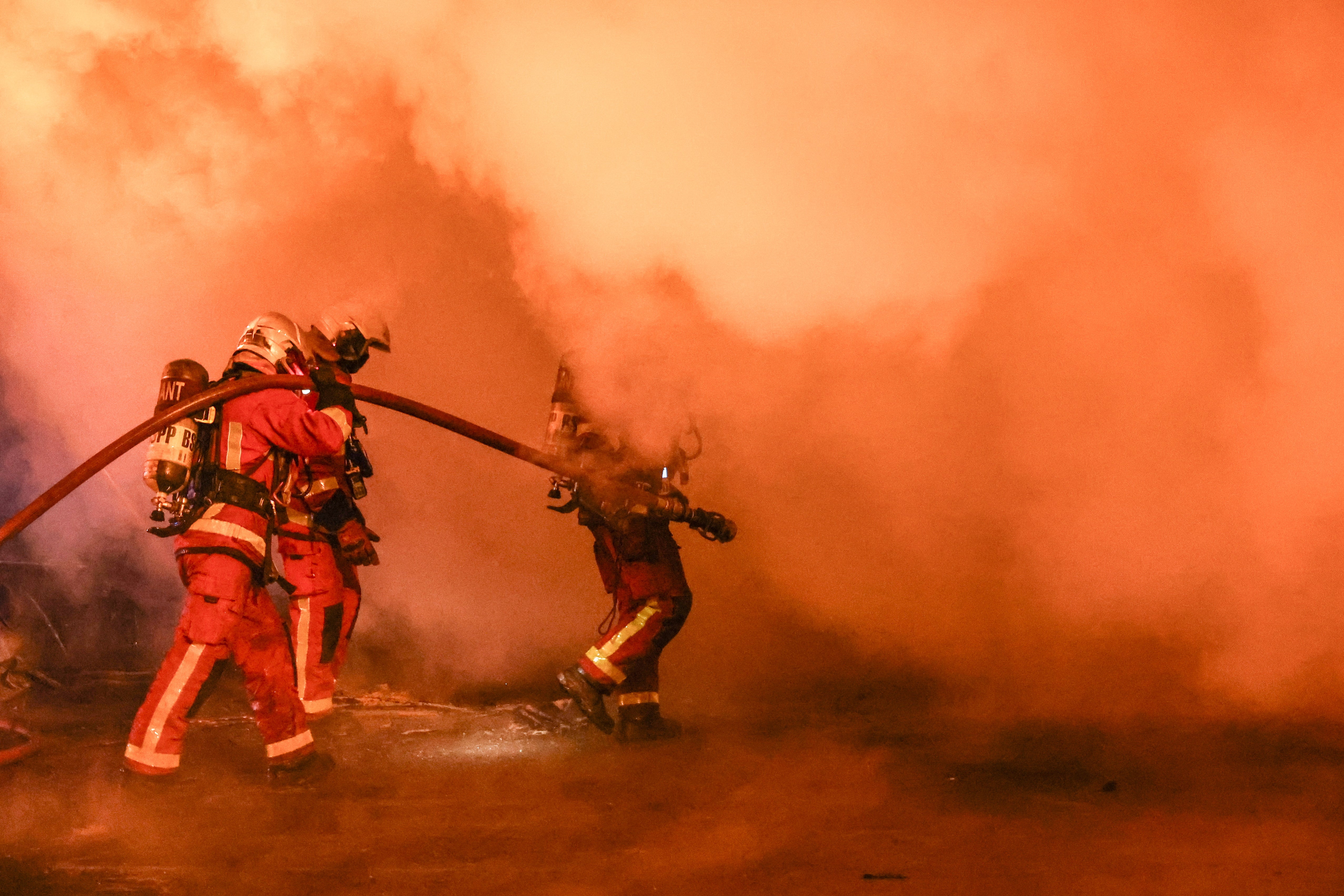 Firefighters extinguish a bus burned during clashes between protesters and riot police in Nanterre on Saturday