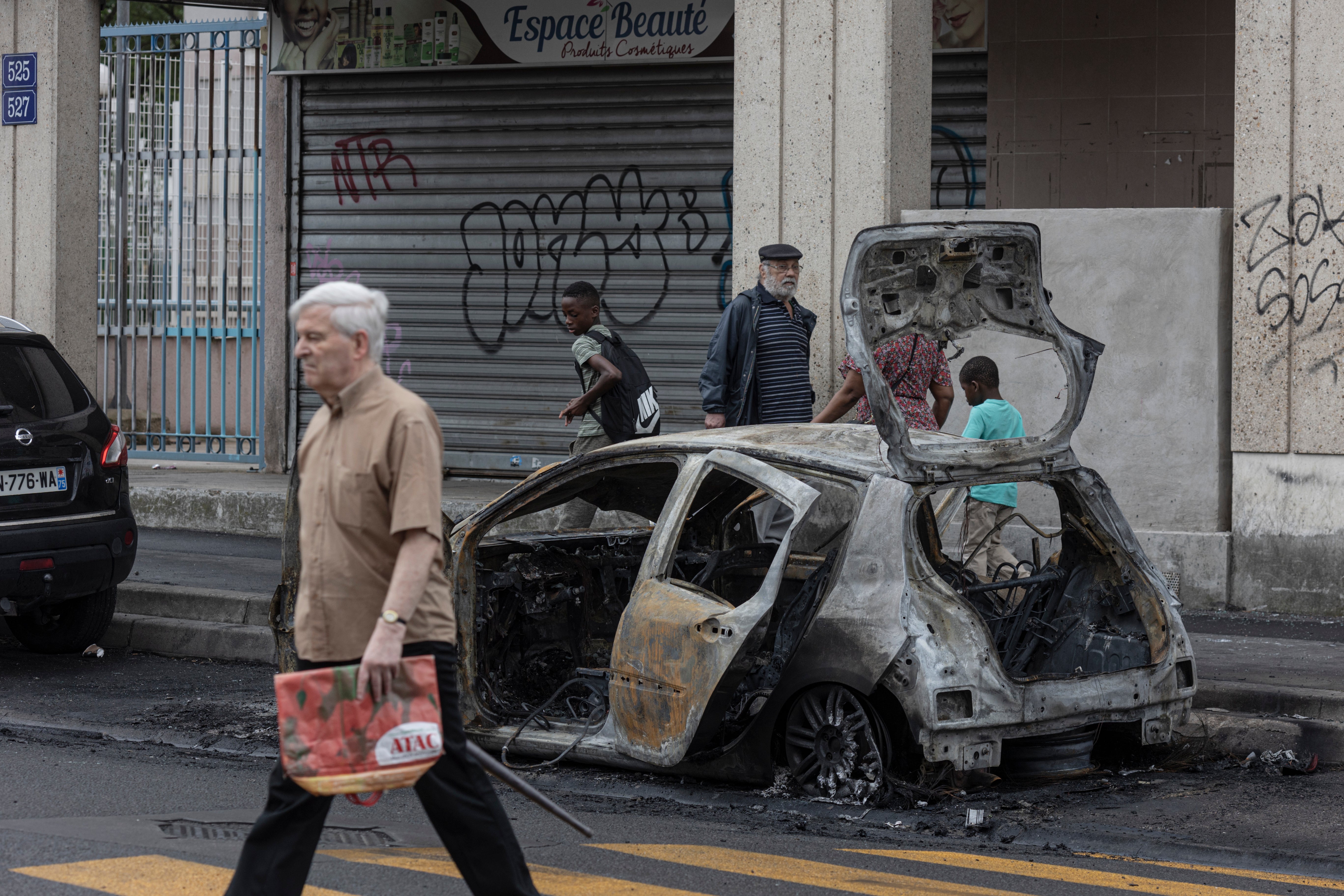 The scorched remains of a car remain by the side of a major roadway follwing rioting