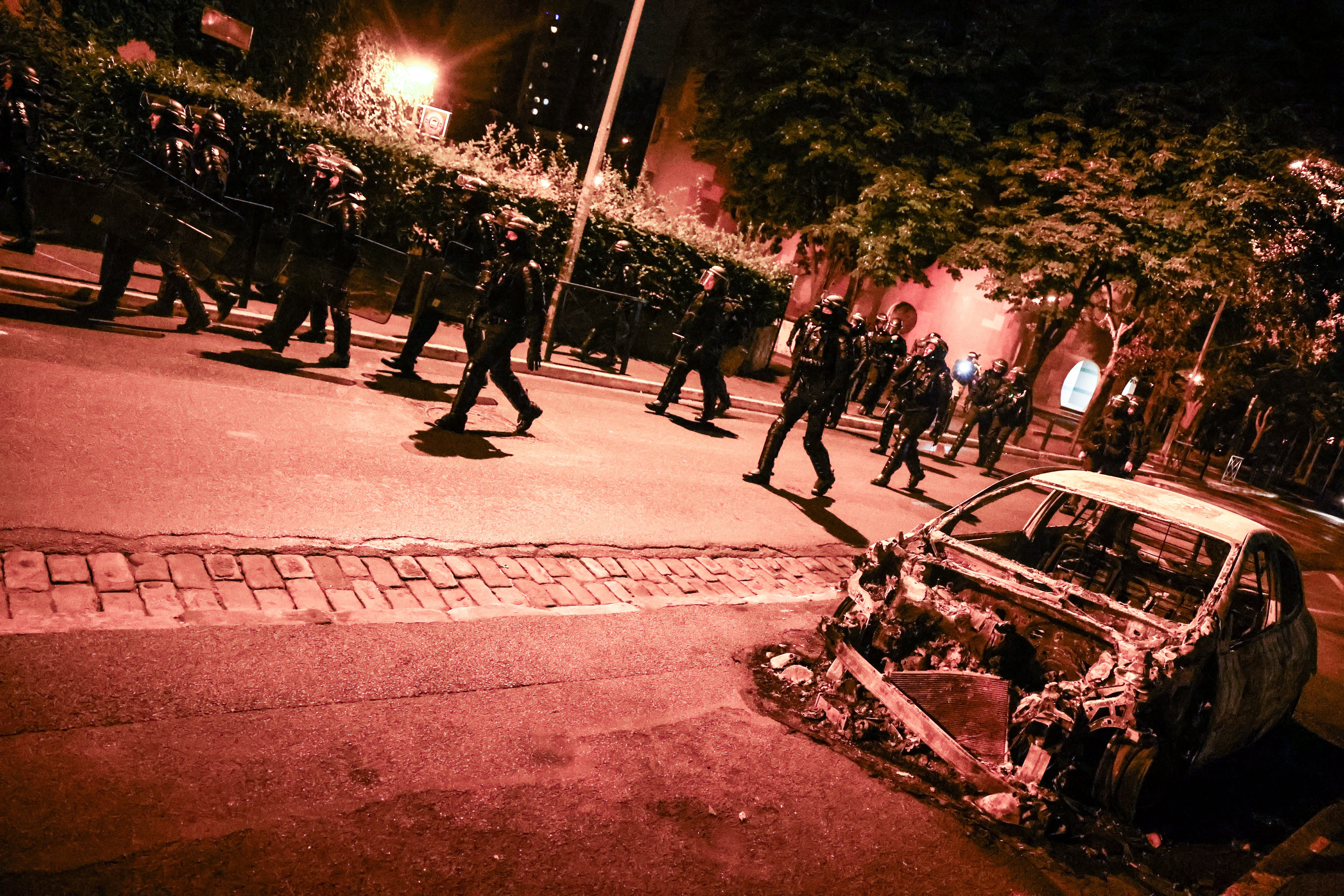 Policemen walk next to a burned car destroyed during clashes between protesters and riot police in Nanterre