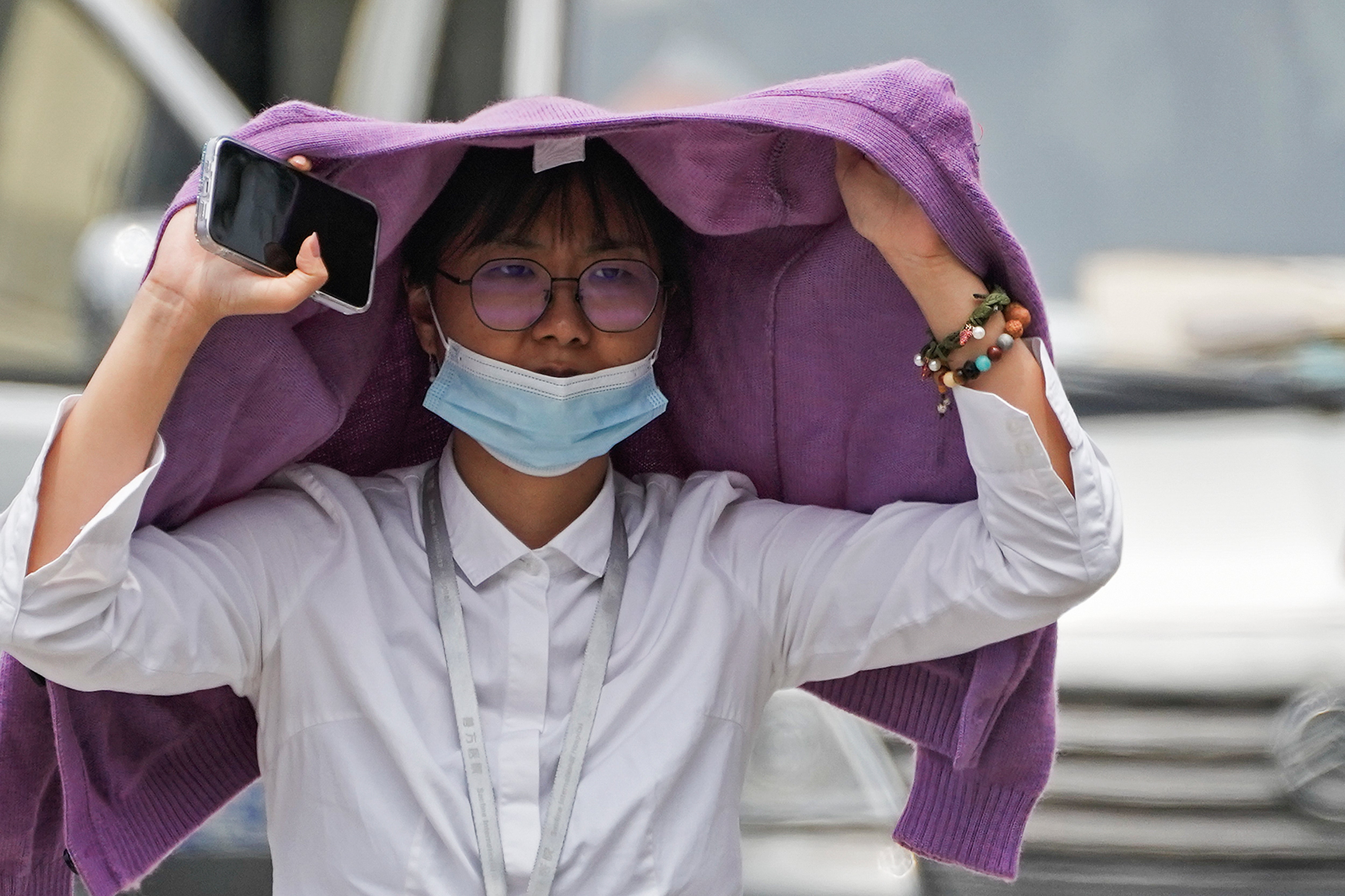 A woman uses a sweater to shield from the sun as she walls on a street on a hot day in Beijing