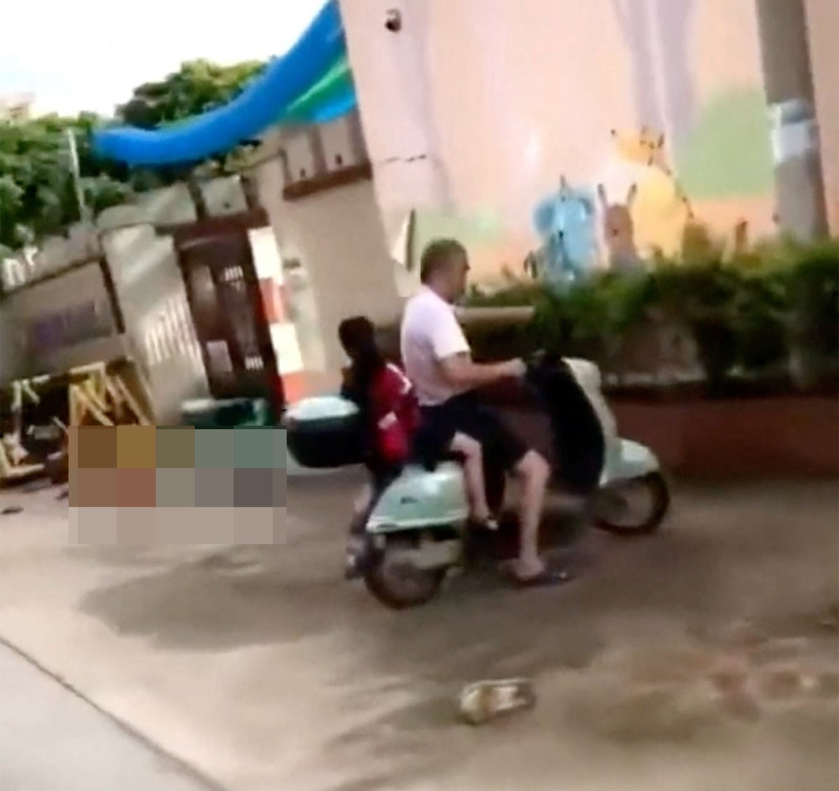 A body lies on the ground near people riding a scooter in the aftermath of a stabbing attack at a kindergarten in Lianjiang county, Guangdong province, China