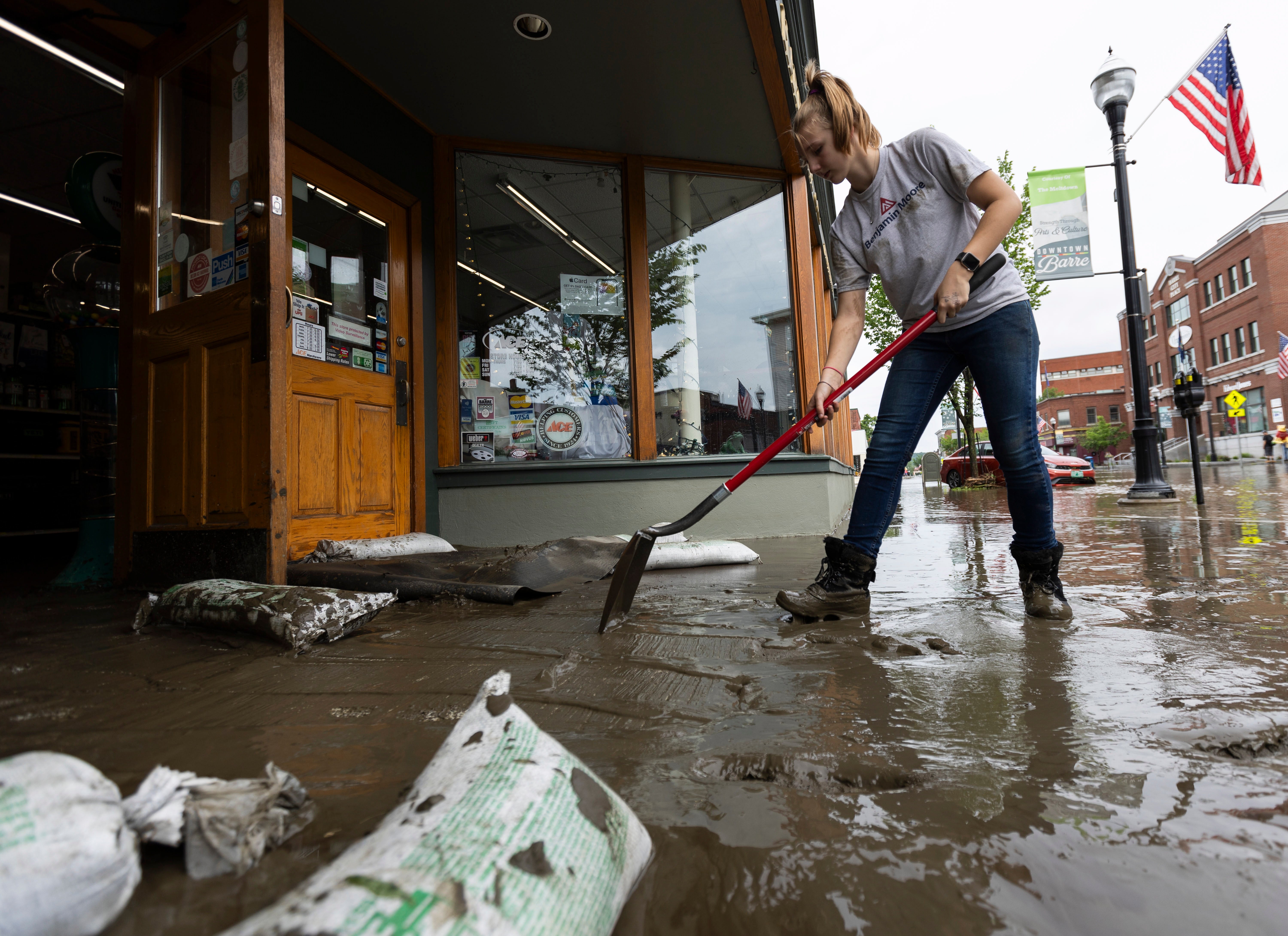 Zyta-Rose Blow, an employee at Nelson Ace Hardware, shovels mud and silt from the shop on Main Street in Barre, Vermont on Tuesday