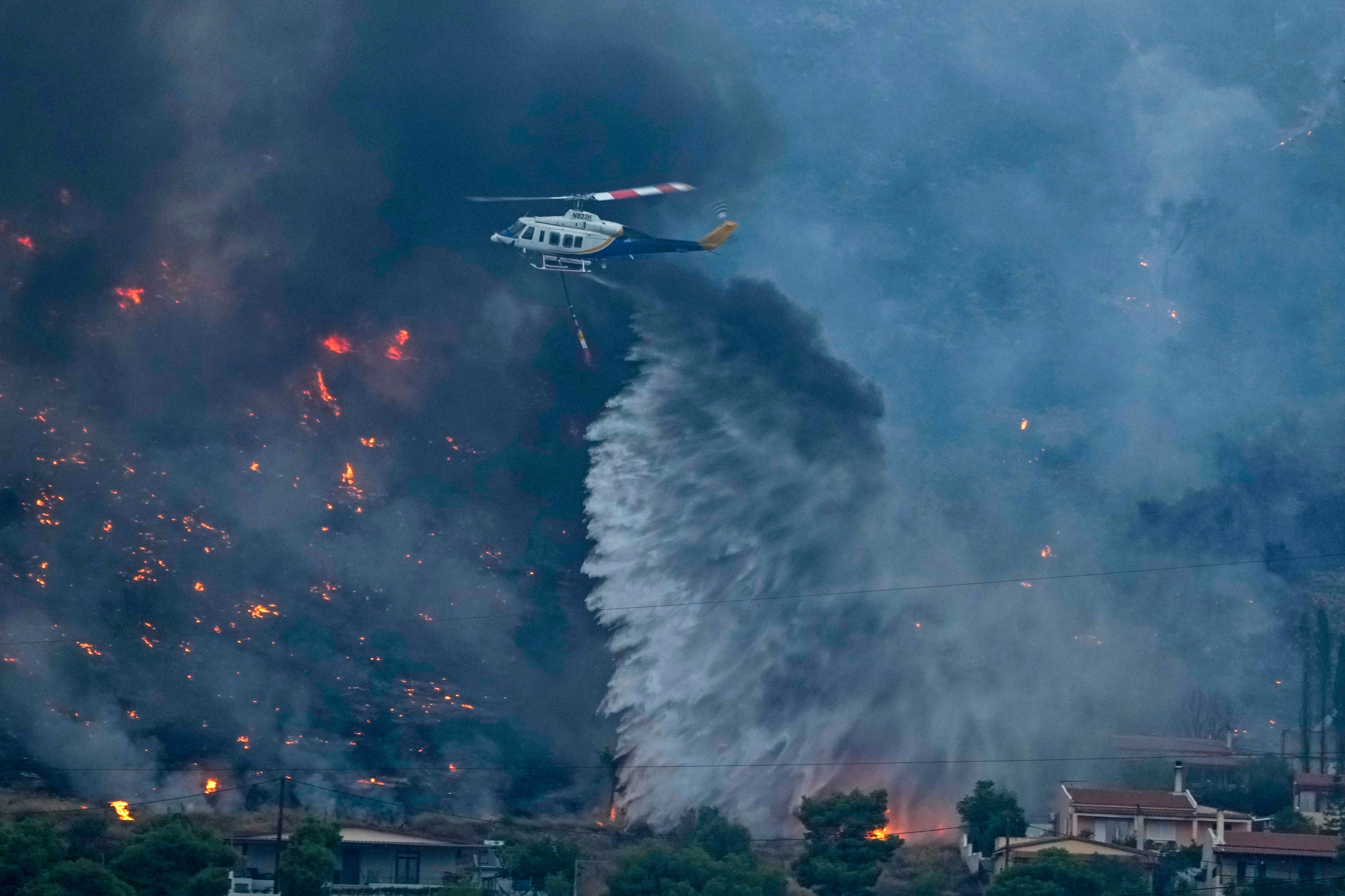 A firefighting helicopter dumps water as fire approach houses in Kalamaki near Agioi Theodori about 60 Kilometres west of Athens , on Monday, July 17, 2023.