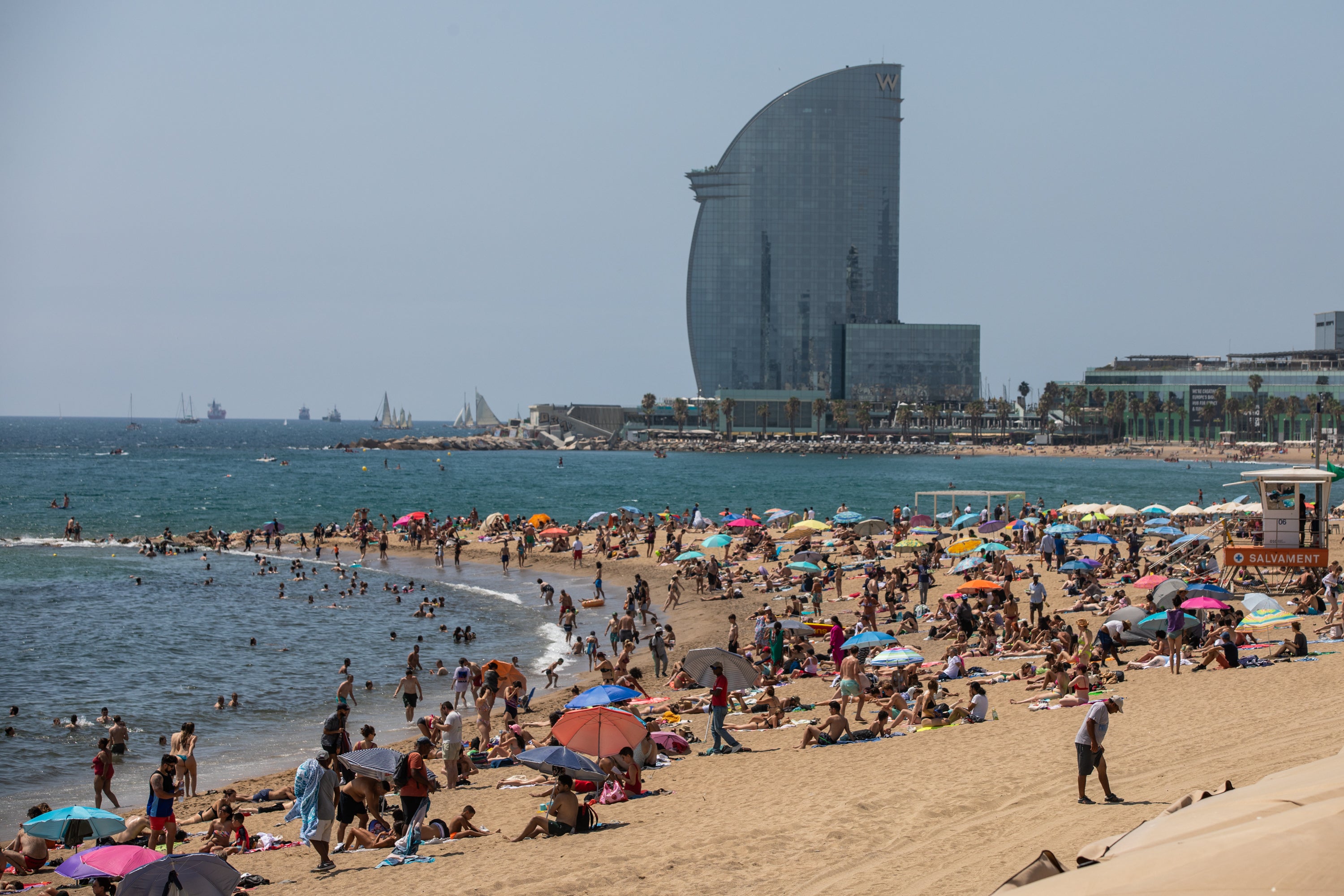 Sunbathers enjoy the sun on Barceloneta beach with the W Barcelona hotel in the background