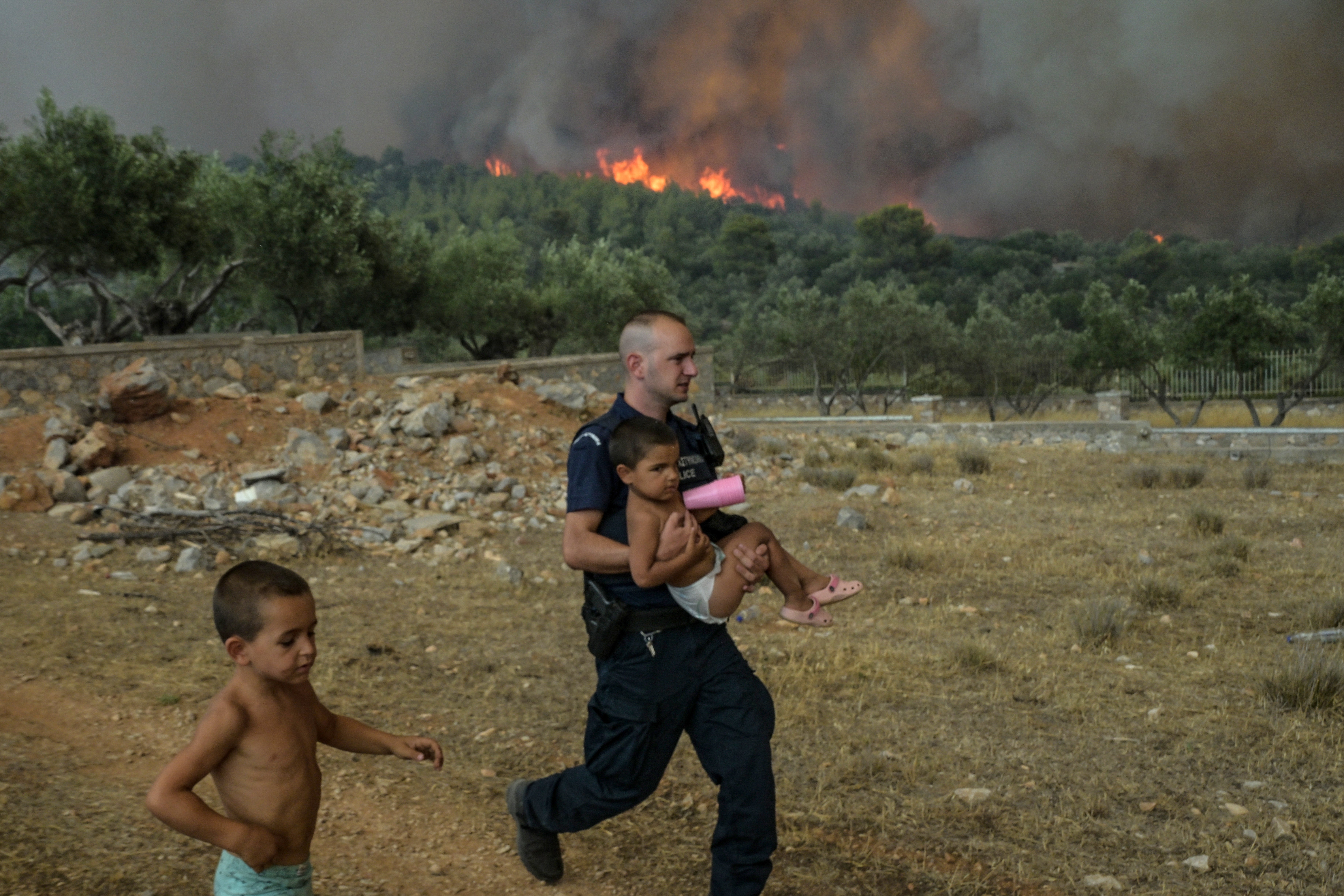 A Greek policeman evacuates a child from wild fire at the village of Agios Charamlabos, near the capital Athens