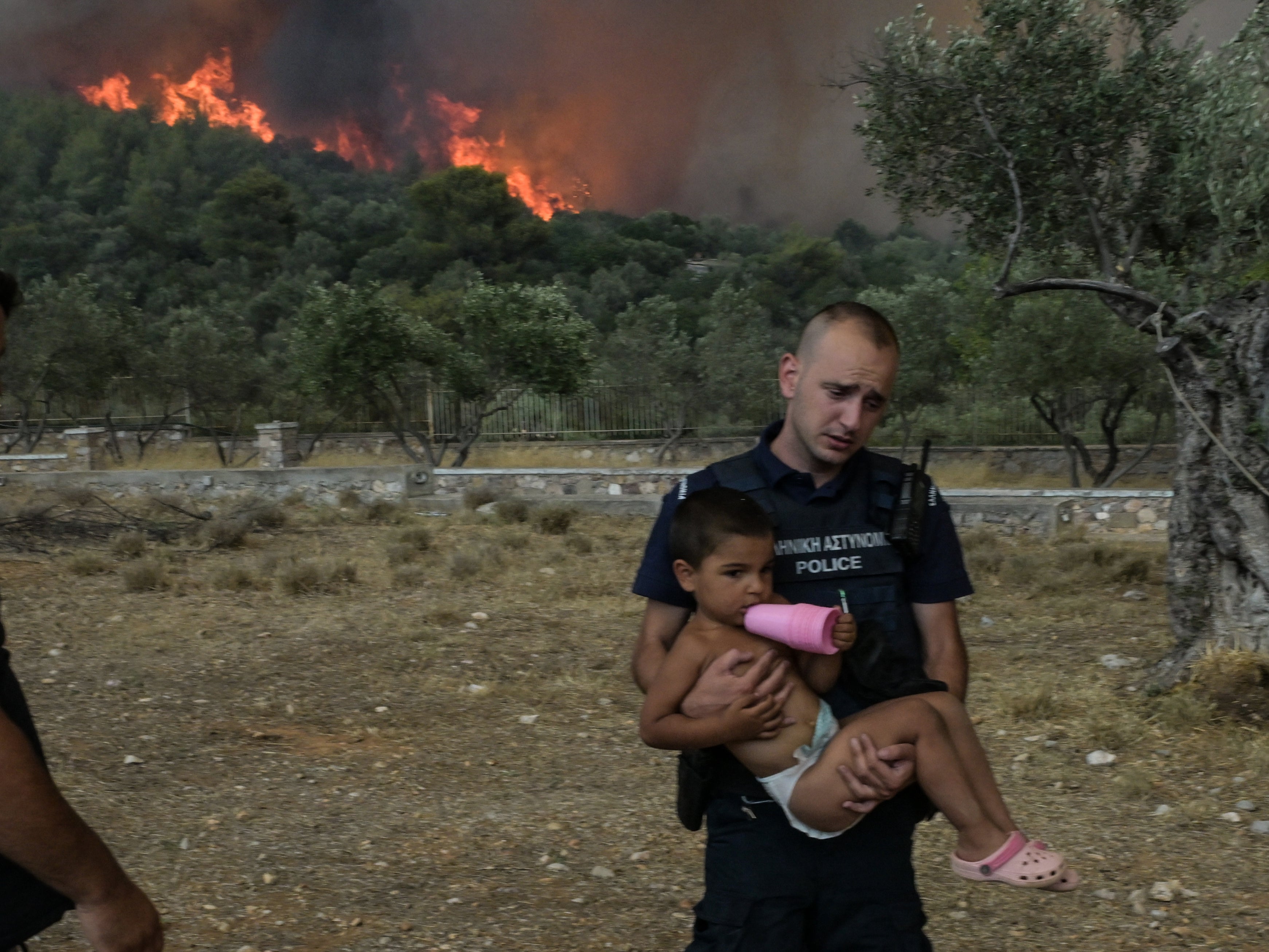 Police officers evacuate children as a wildfire burns, in the village of Agios Charalampos, near Athens, on July 18, 2023