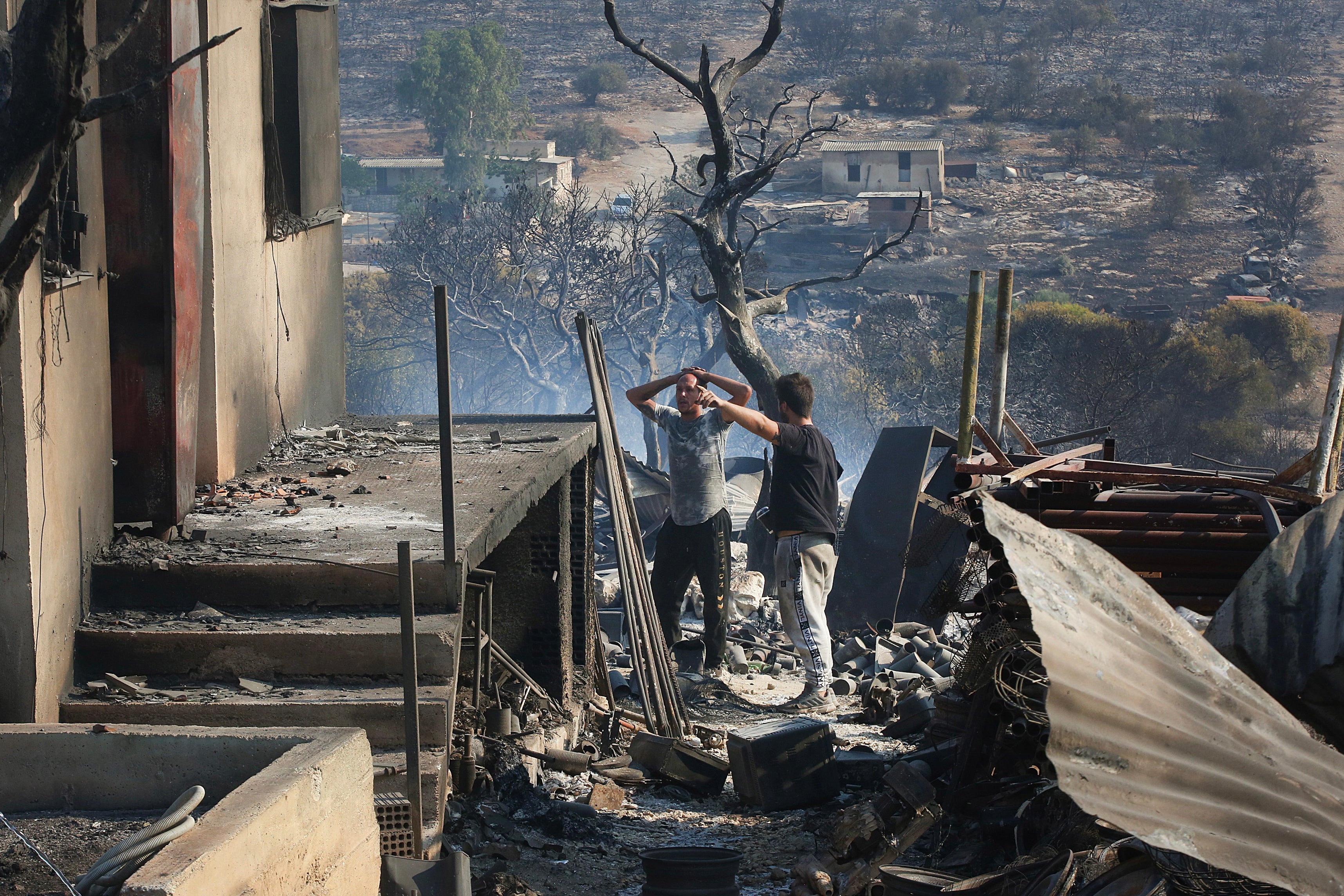 Residents look in despair at their house which has been completely destroyed due to a wildfire, in Dervenochoria, northwest of Attica region, Greece.