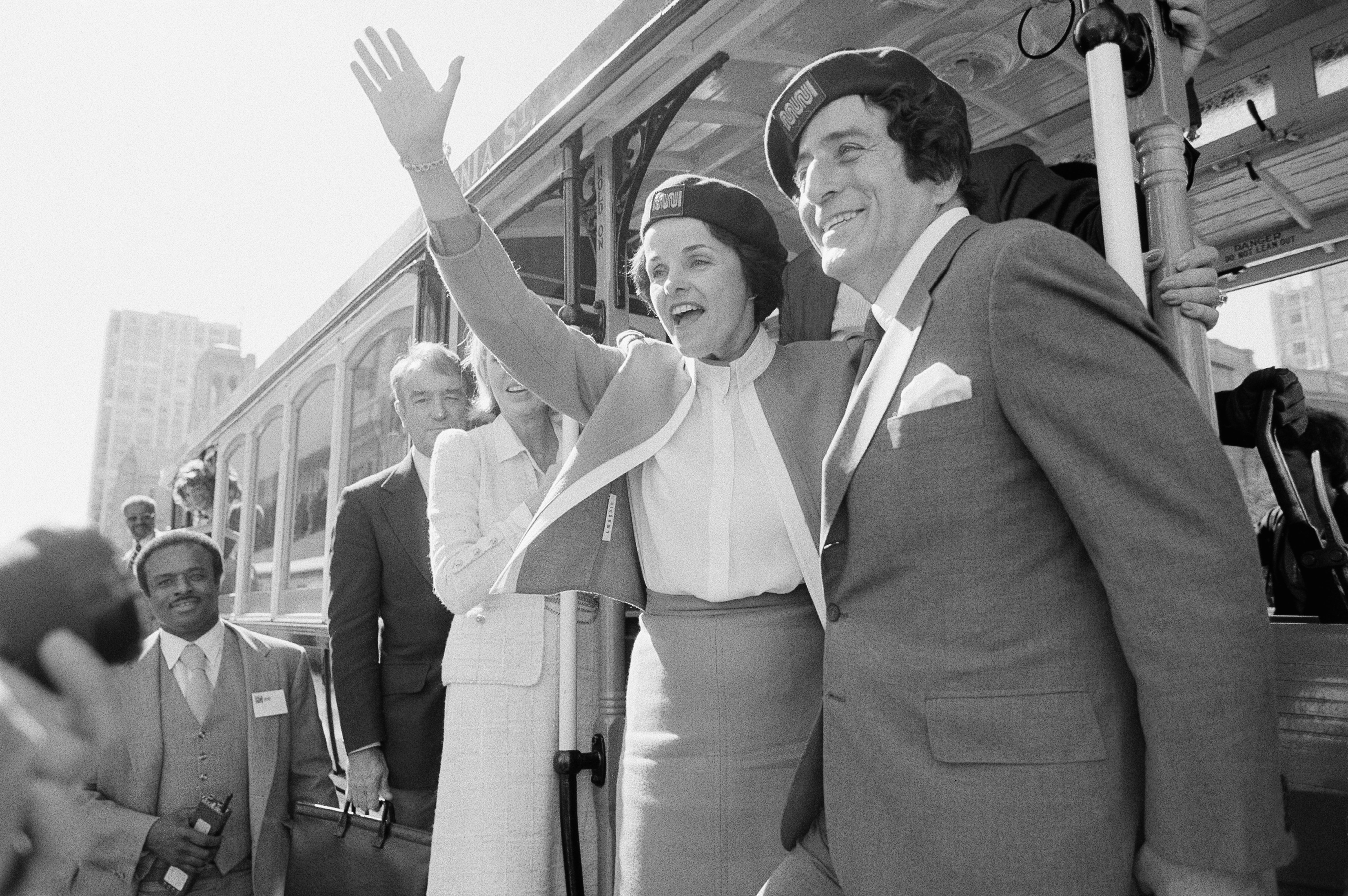 The then San Francisco Mayor Dianne Feinstein and singer Tony Bennett, who sang " I Left My Heart in San Francisco," hangs on to the outside of a cable car in San Francisco before taking a test ride, Wednesday, May 2, 1984