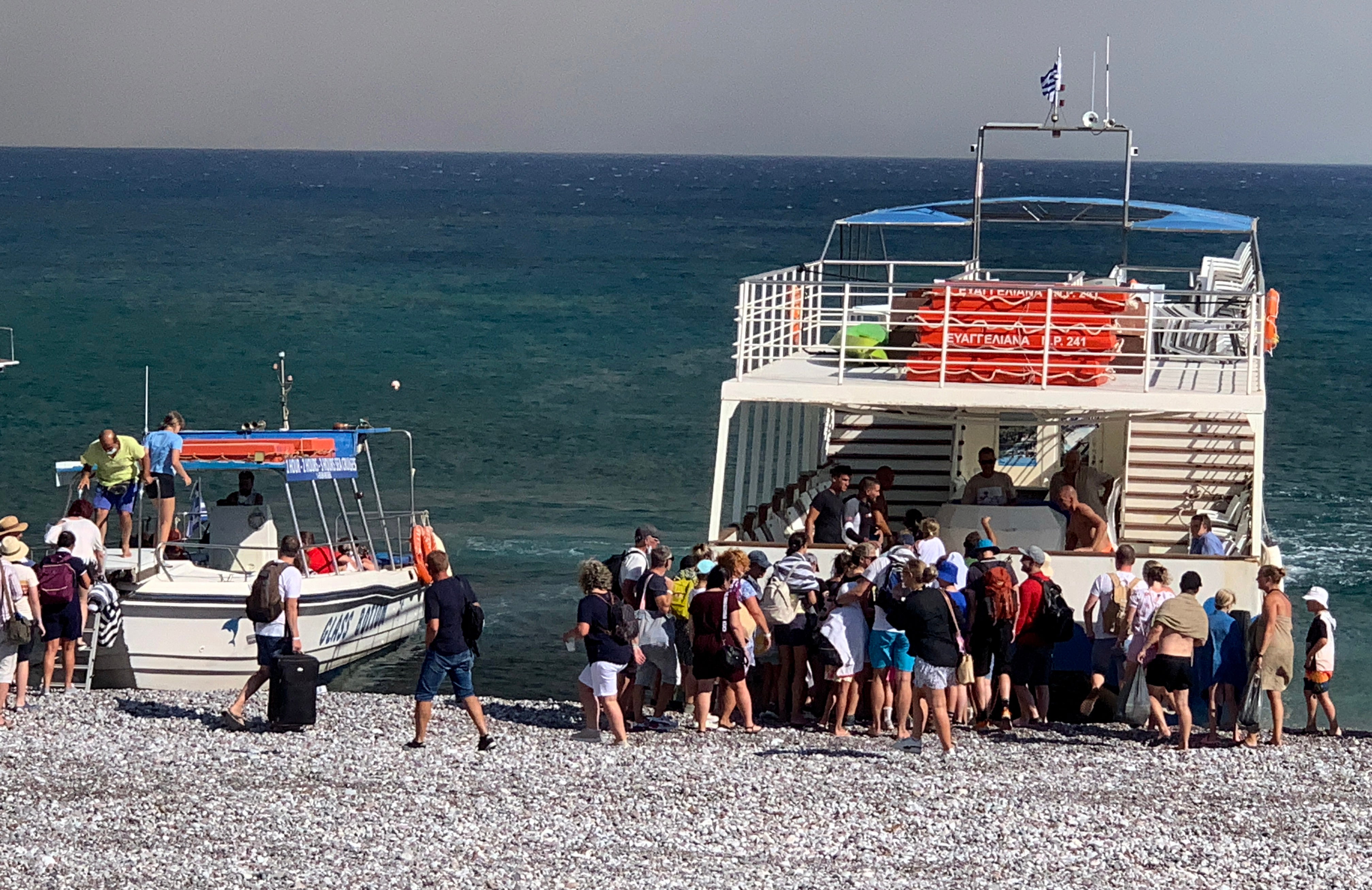 Tourists stand on a beach after being evacuated during a forest fire on the island of Rhodes