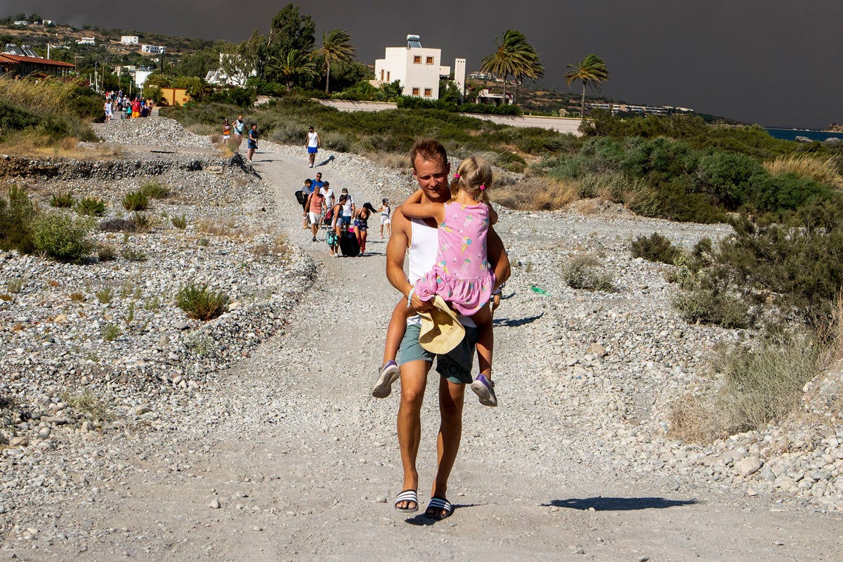 A man carries a child as they leave an area where a forest fire burns, on the island of Rhodes, Greece, Saturday, July