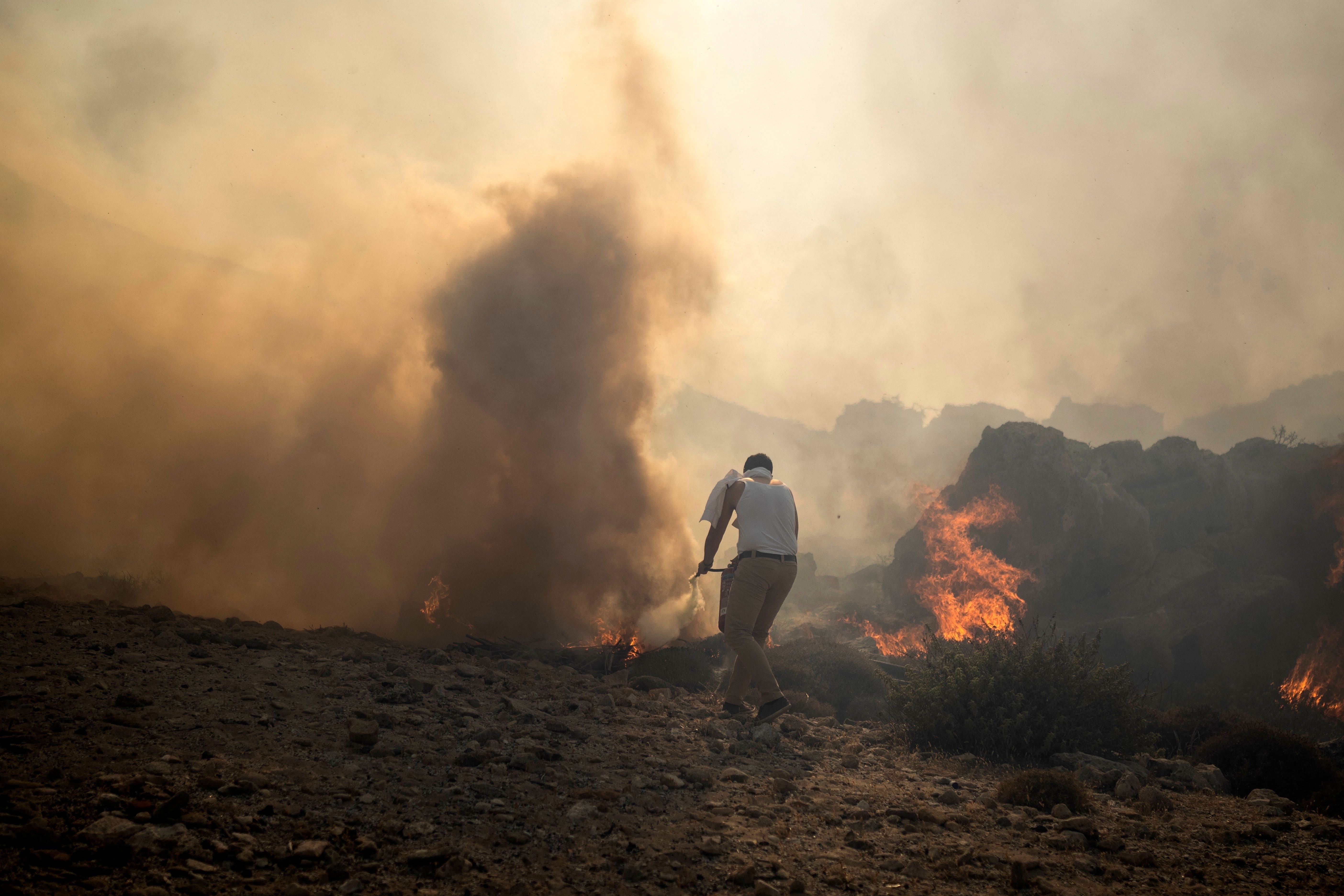 A local resident tries to extinguish a fire, near the seaside resort of Lindos (AP Photo/Petros Giannakouris)