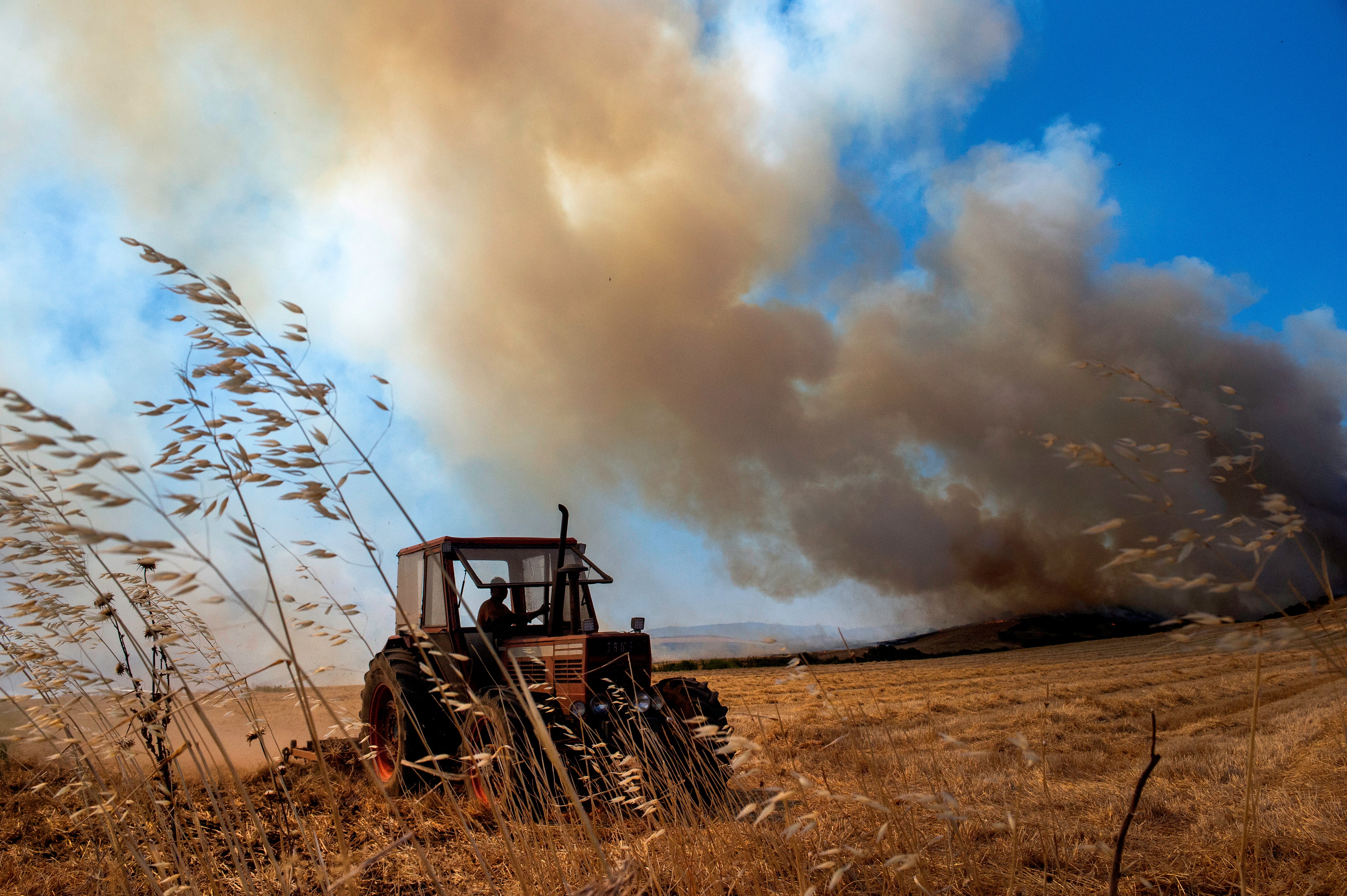 A farmer operates a tractor during a wildfire in Velestino, Magnesia prefecture