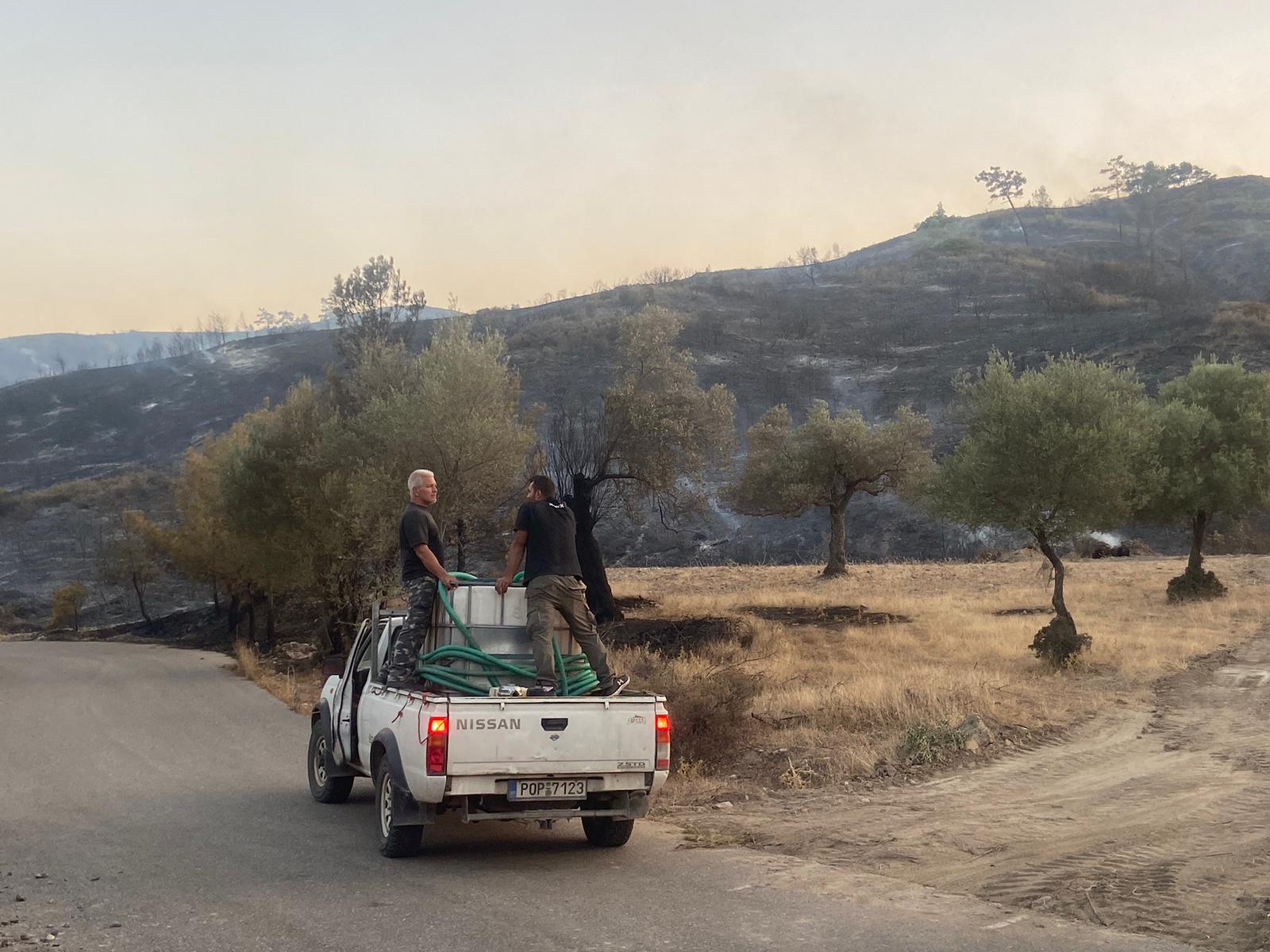 Volunteer firefighters survey the charred remains of trees which could smoulder for days near Vati