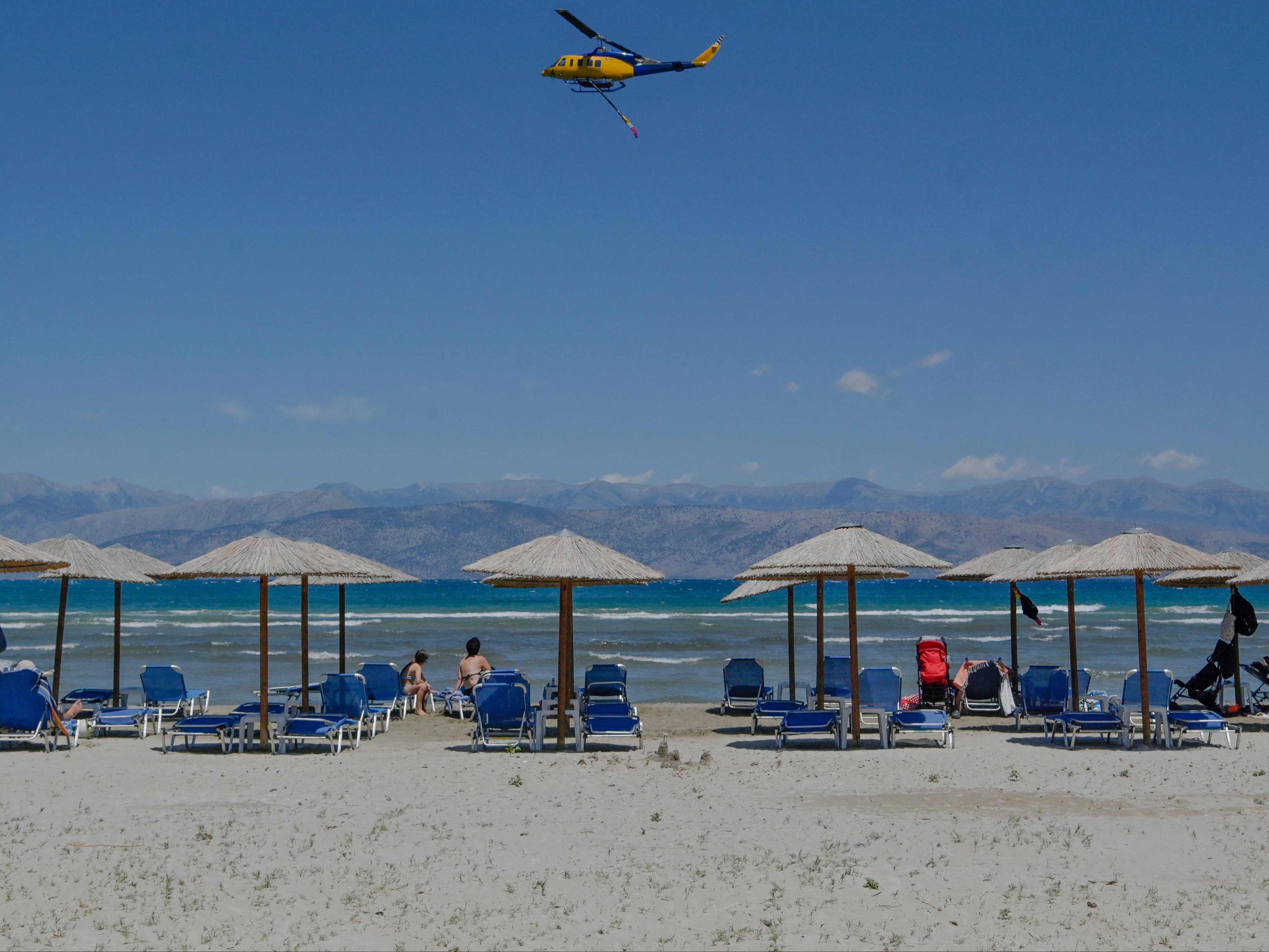 A firefighting helicopter flies past holidaymakers lining the beachfront, after making a water drop on wildfires near the village of Loutses on the Greek island of Corfu, on July 27, 2023