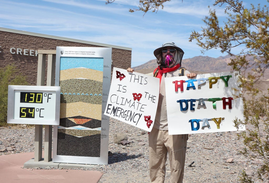 A protestor stands next to a digital display of an unofficial heat reading at Furnace Creek Visitor Center in Death Valley, California