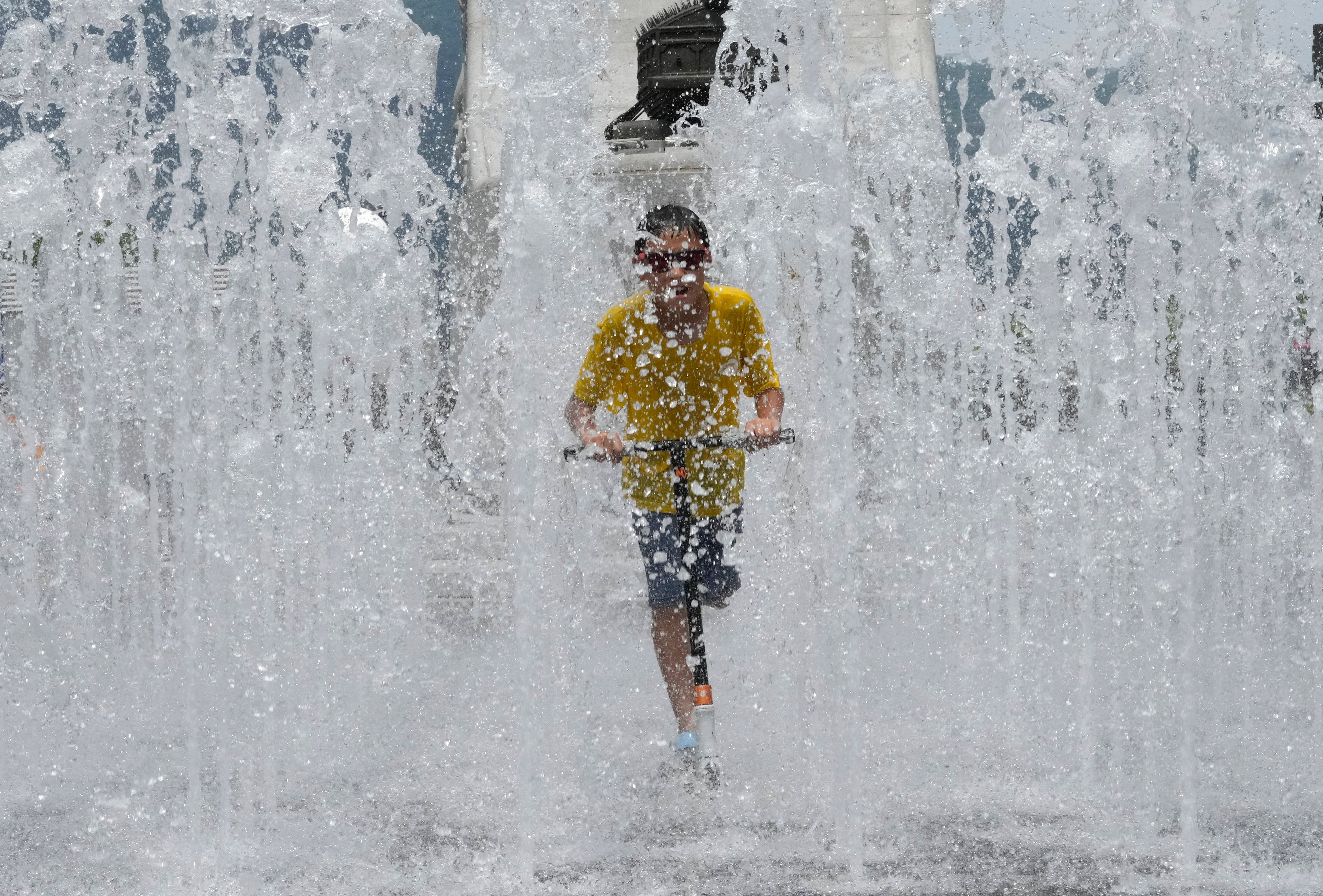 A boy rides a scooter through a fountain in Seoul, South Korea