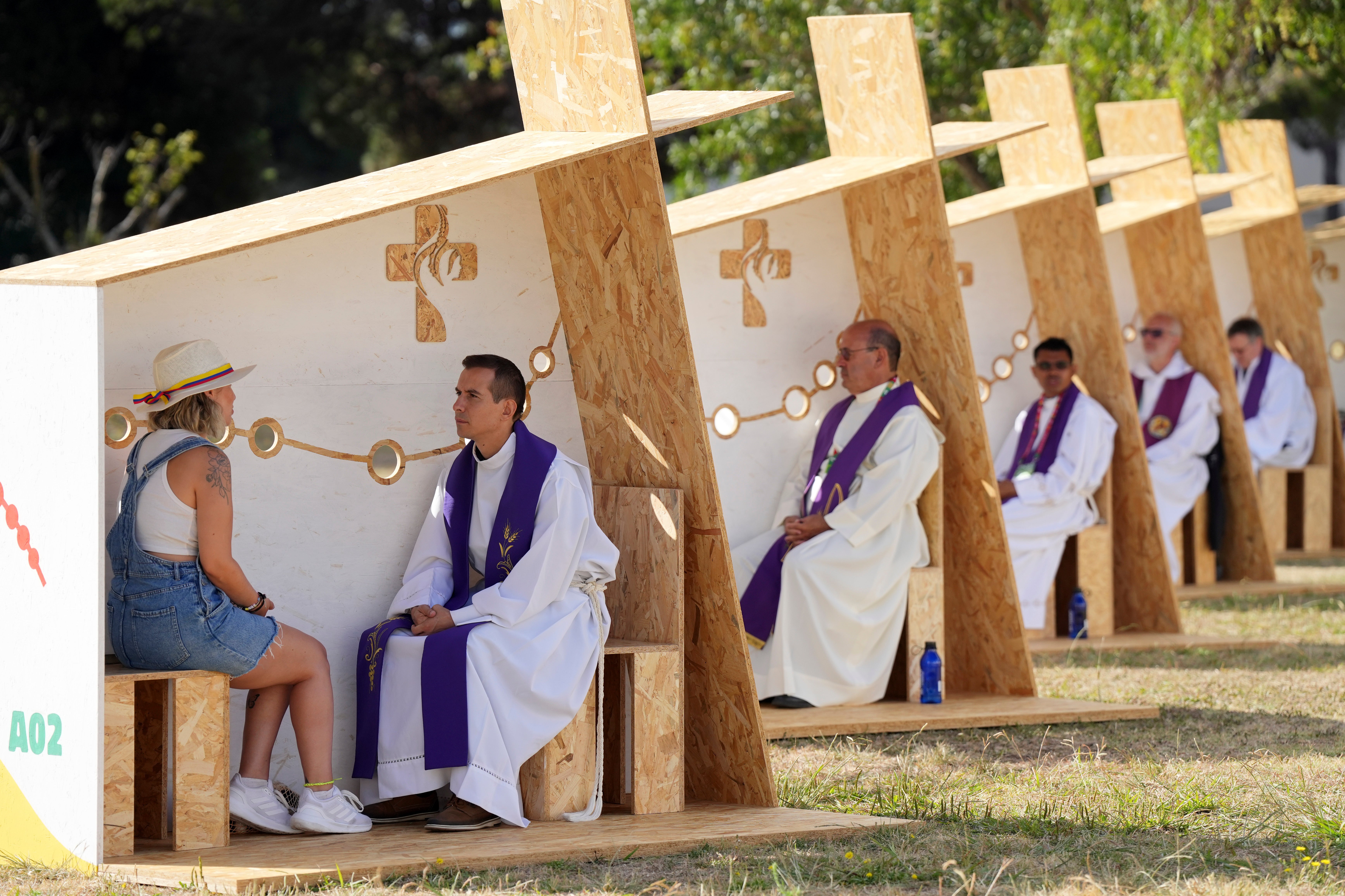 A priest listens to confession in a row of confessionals set up for pilgrims arriving for international World Youth Day at a park in Lisbon