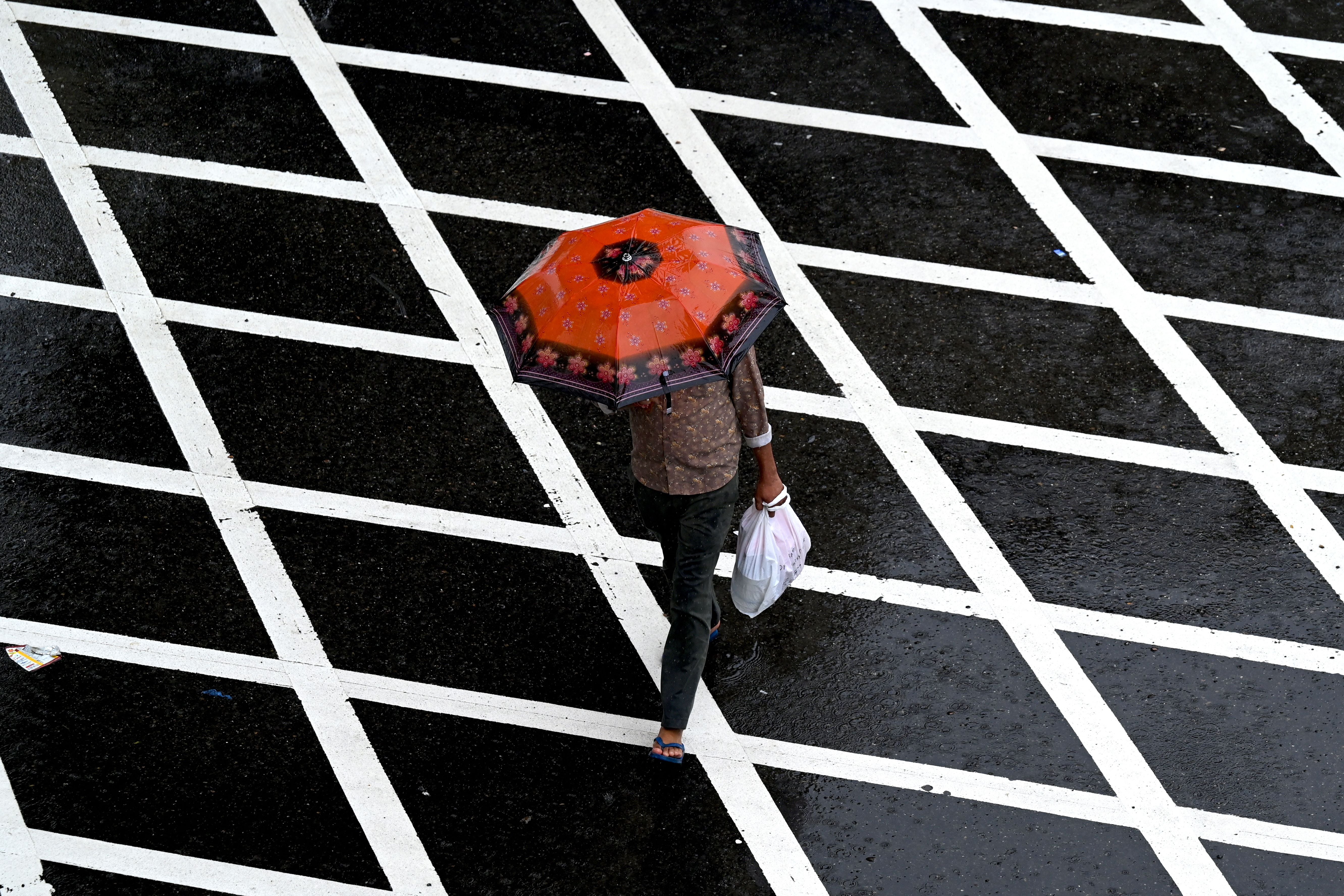 A pedestrian walks across a street during rainfall in Mumbai