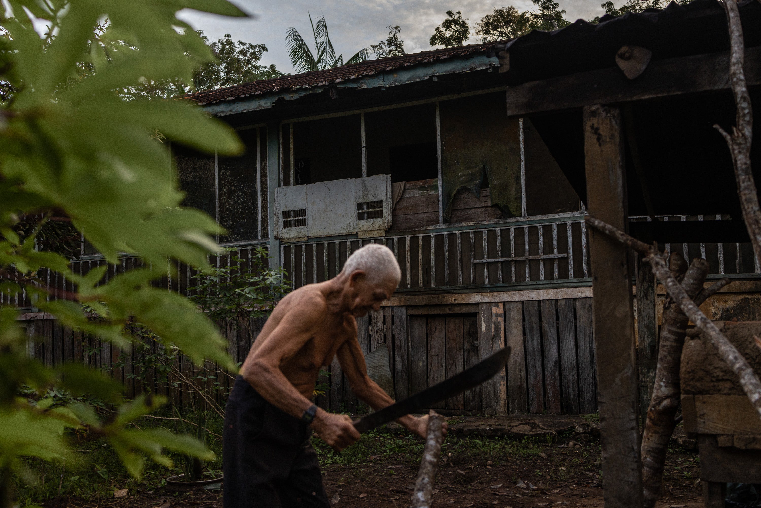 Elizeu Couto Nogueira, 78, chops wood for cooking behind the house where he lives in the deteriorating American village