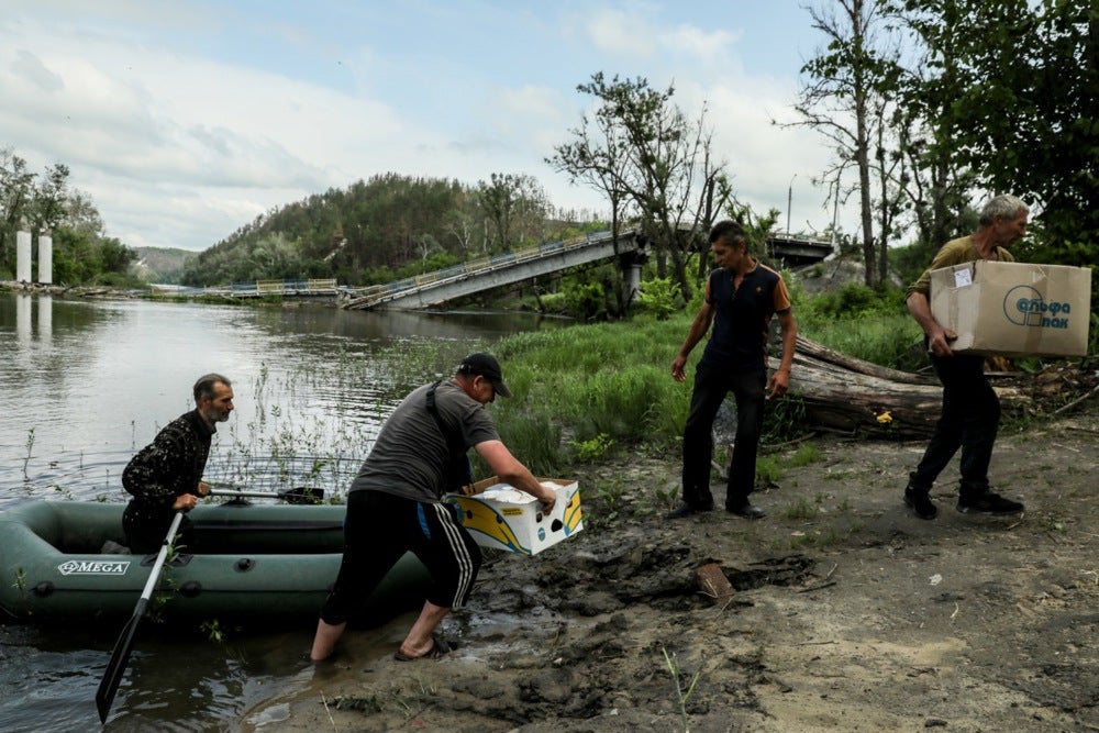 Mykola next to local residents carrying boxes with hot meals, brought by volunteers