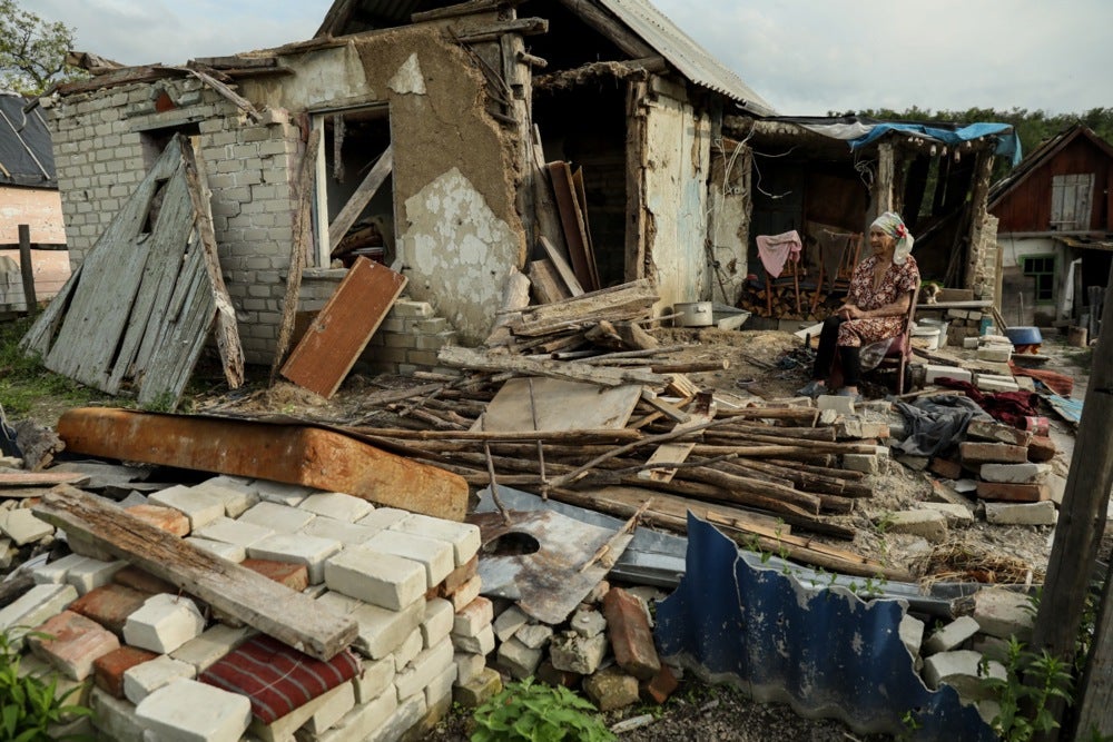 Mykola’s mother, Nina, sits on a chair amid the remains of her house