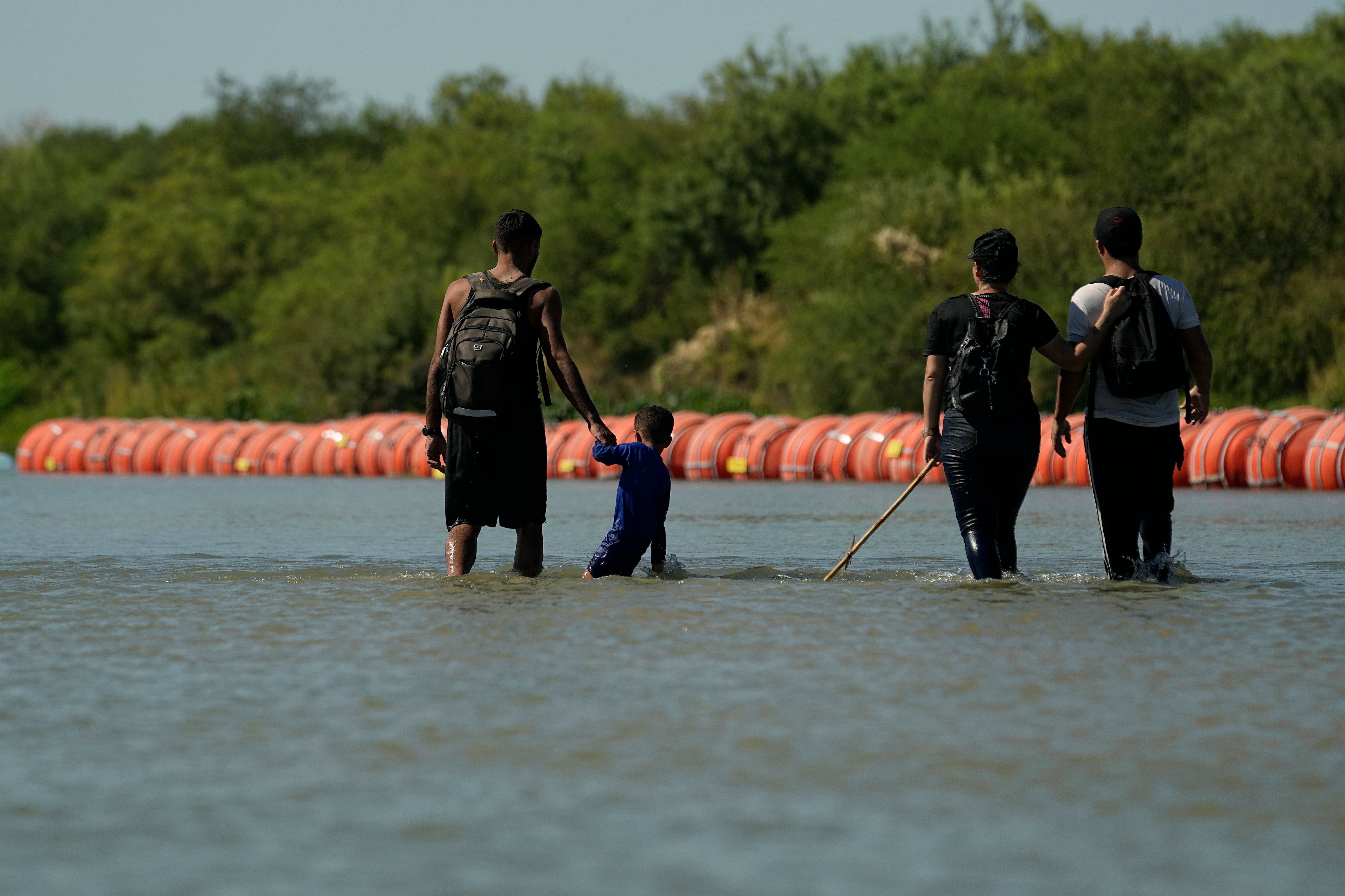 Migrants crossing into the US from Mexico walk along large buoys being used as a floating border barrier on the Rio Grande in Eagle Pass, Texas