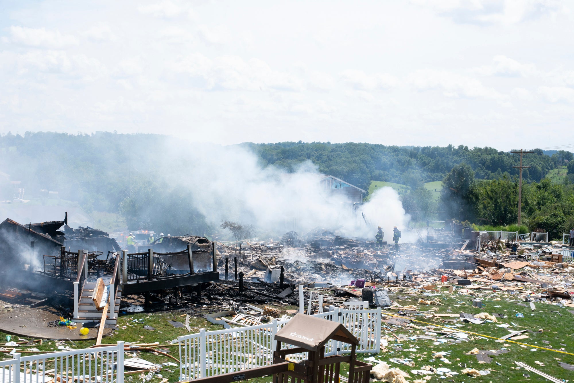 Two firefighters stand on the debris around the smoldering wreckage of the the three houses