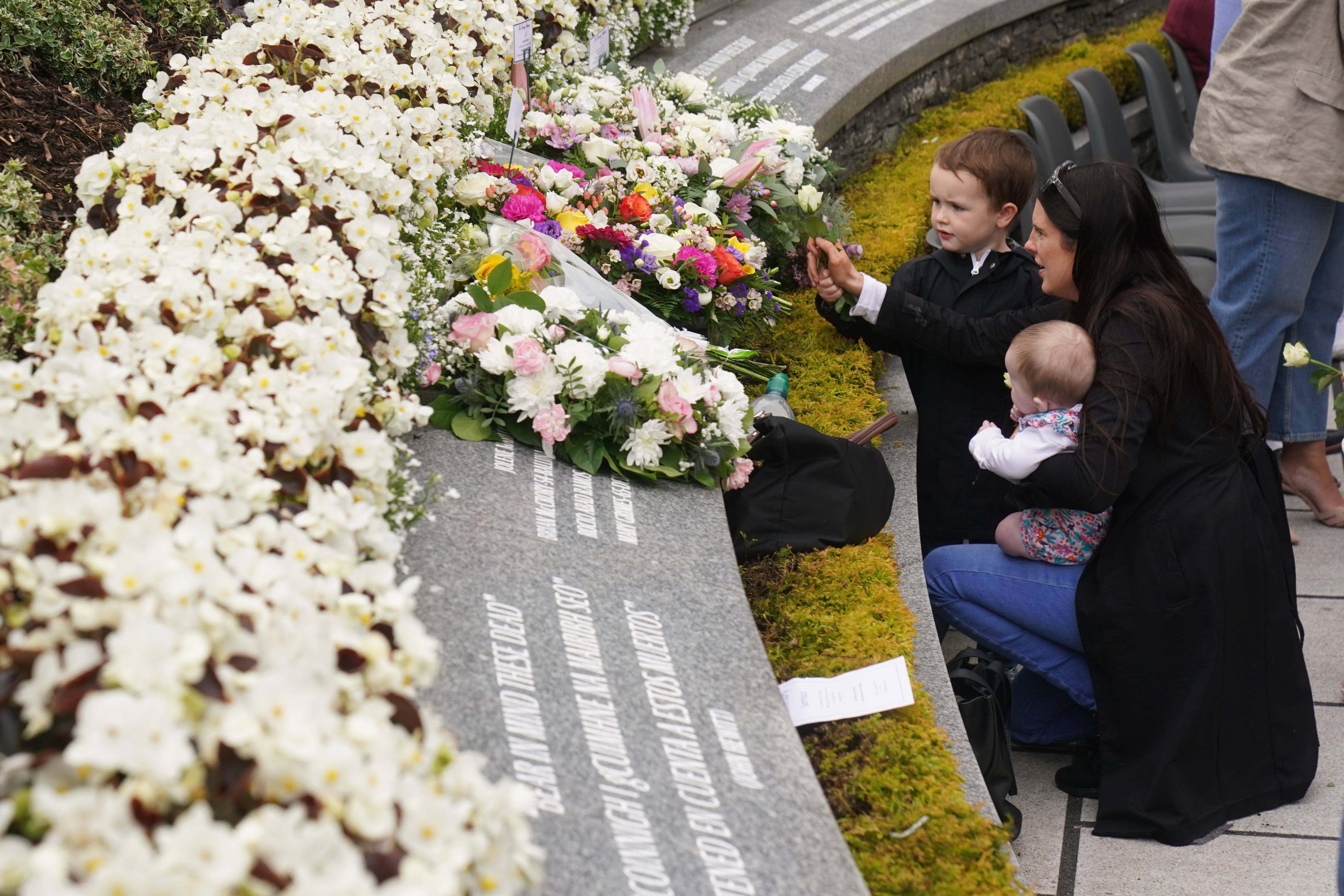 Bernadette Duffy (right) with son Daithi, aged four, and daughter Saoirse, aged four months, place a flower during a service to mark the 25th anniversary of the bombing that devastated Omagh in 1998 (Brian Lawless/PA)