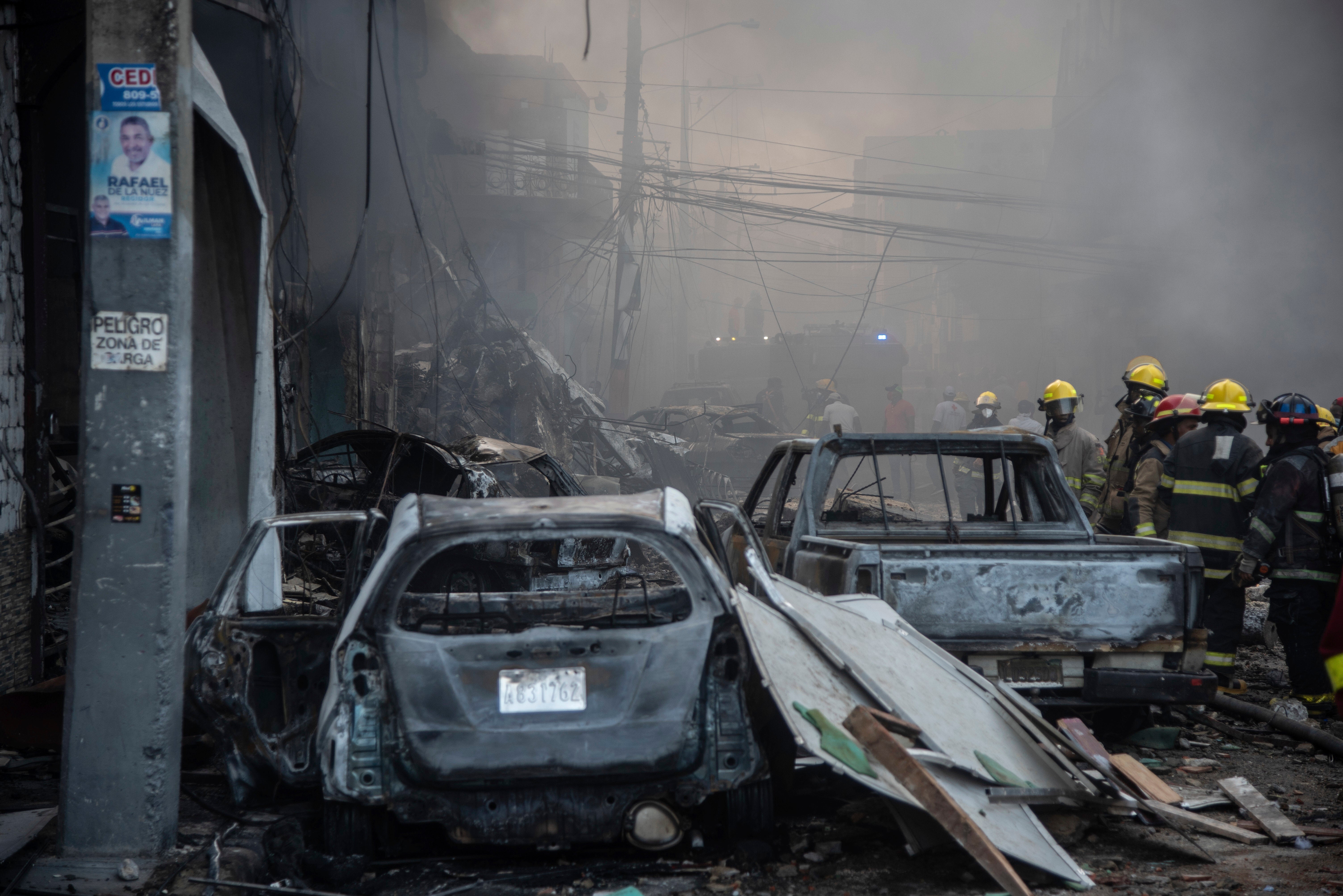 Firefighters work next to destroyed vehicles after a powerful explosion in San Cristobal, Dominican Republic, Monday, Au...