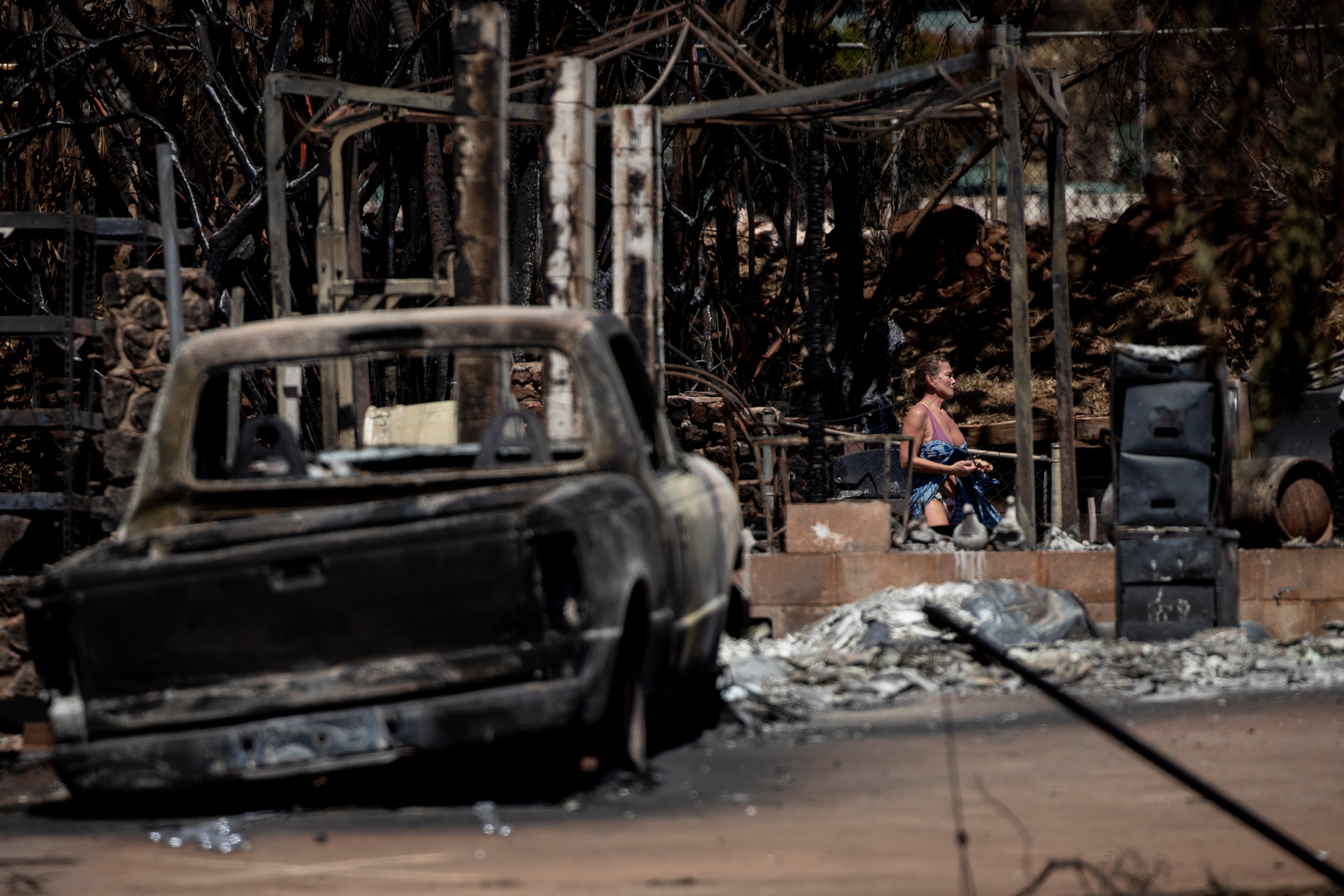 A resident walks through the ruins of a house destroyed by the Lahaina Fire