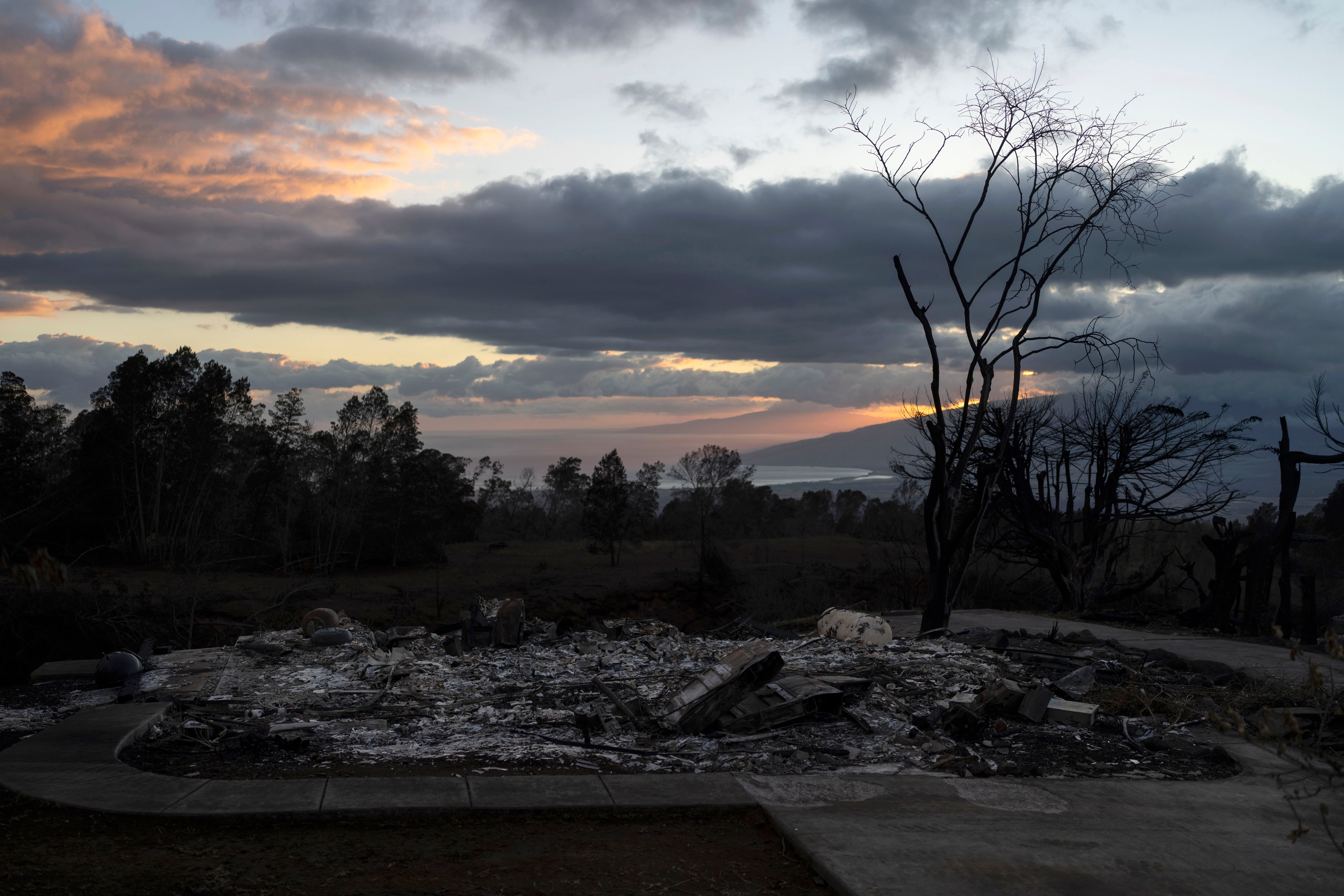 A home burned to ashes is seen in foreground as the sunset colors the sky in Kula, Hawaii, Tuesday, Aug. 15, 2023,