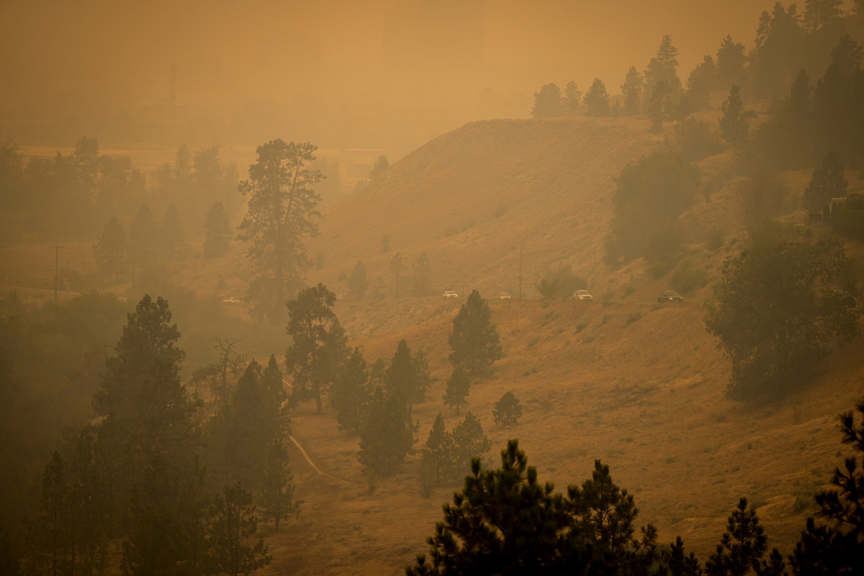 Smoke from wildfires fills the air as motorists travel on a road on the side of a mountain, in Kelowna, British Columbia