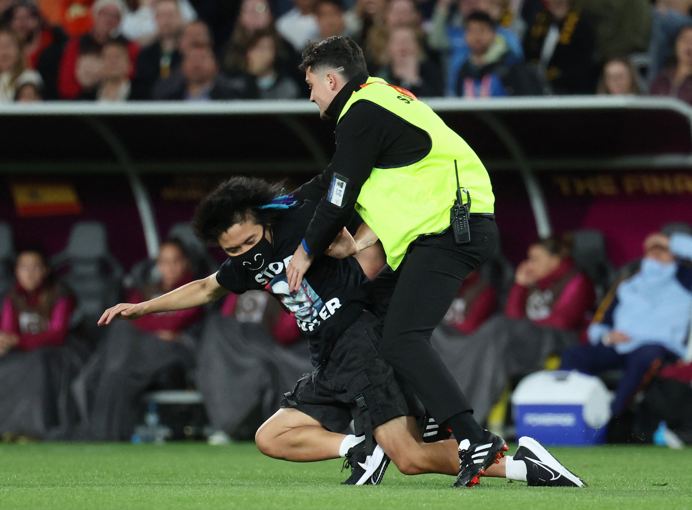 A pitch invader wearing a T-shirt protesting against Russia’s president Vladimir Putin is detained by a steward