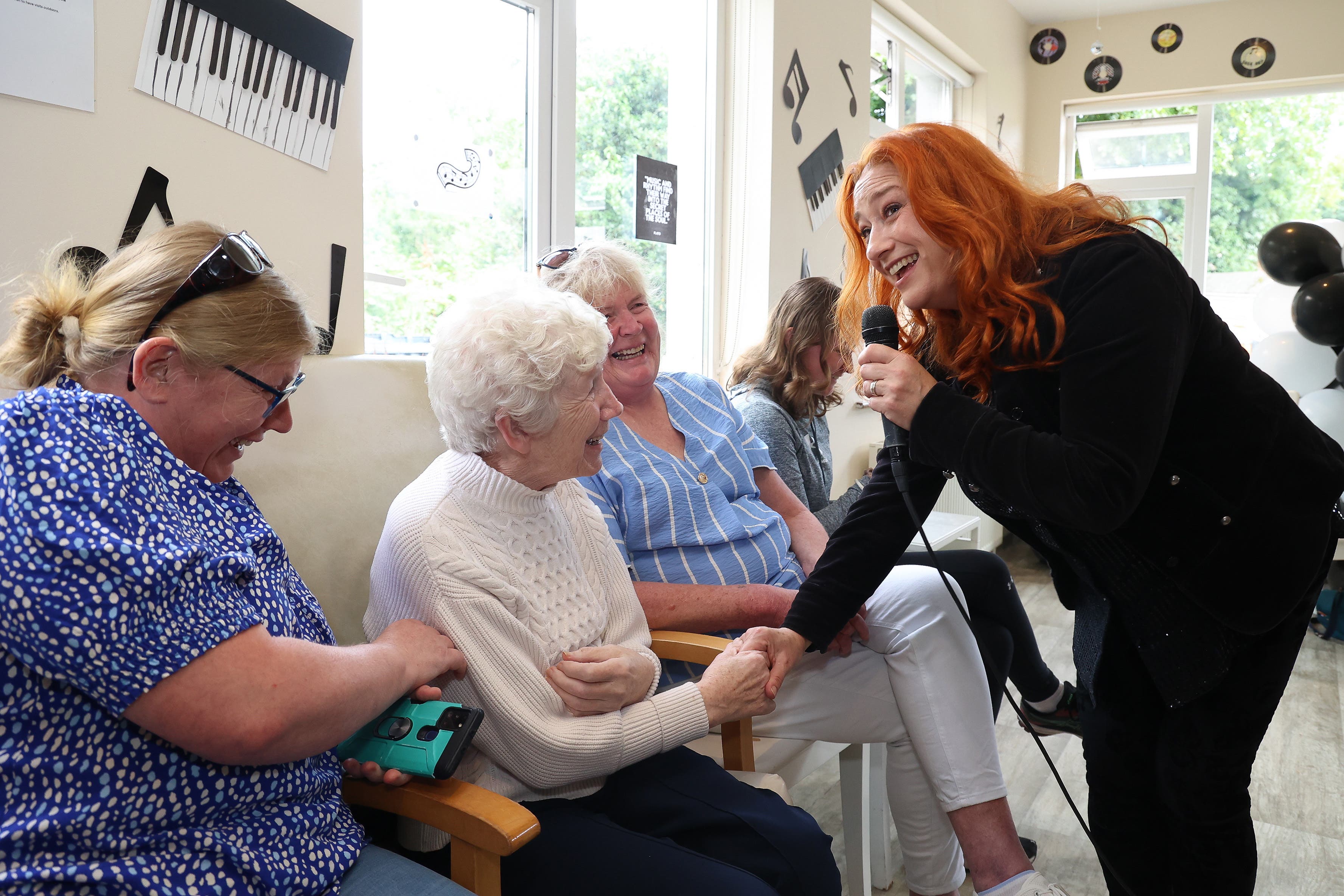 Agnus McCabe with her daughters, Roisin and Siobhan, listen to Niamh Kavanagh and the Mobile Music Machine perform at Asgard Lodge Nursing Home in Arklow, Co Wicklow (Julien Behal Photography/PA)