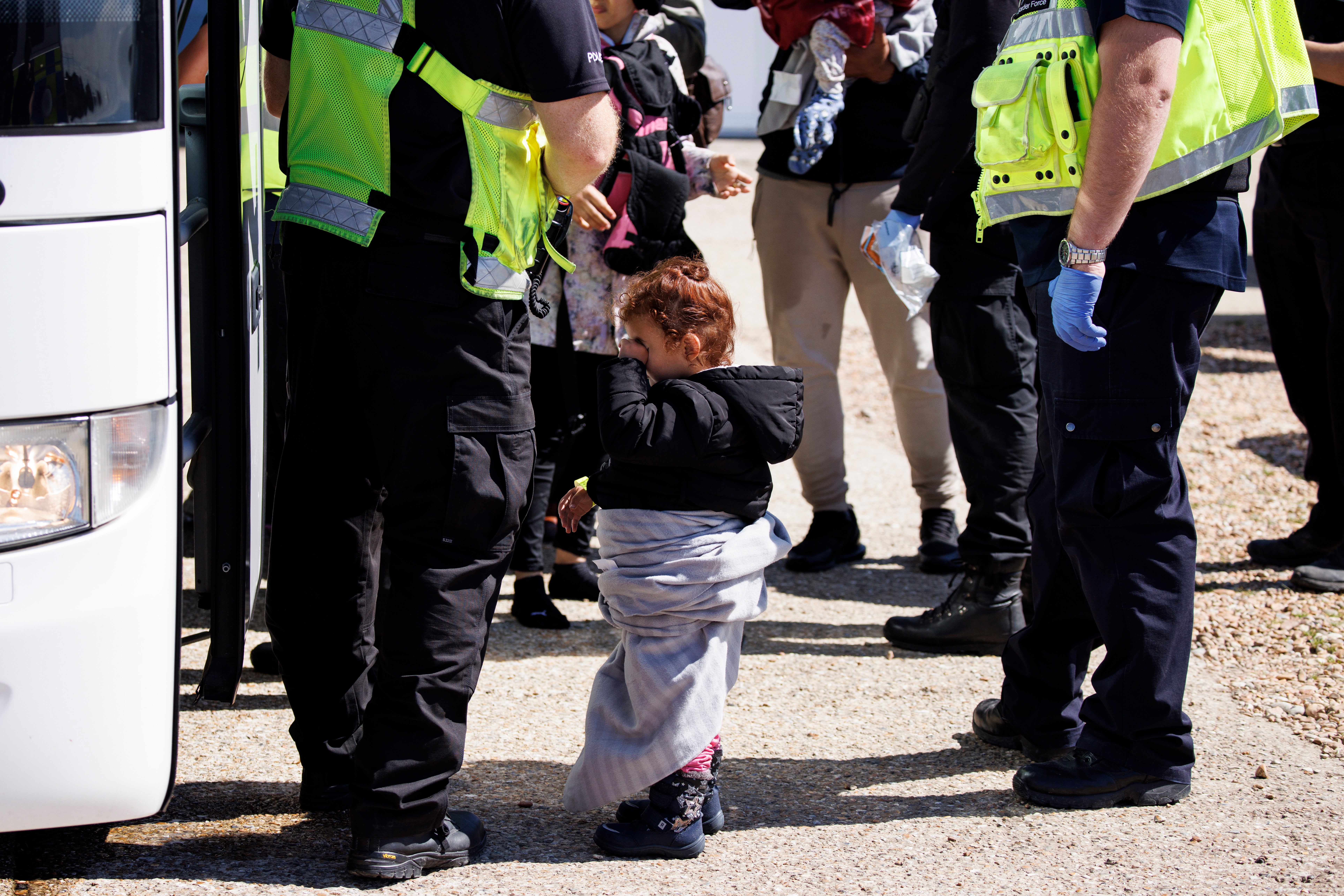 A child rescued from a boat crossing the English Channel is taken to a Home Office bus on Dungeness Beach