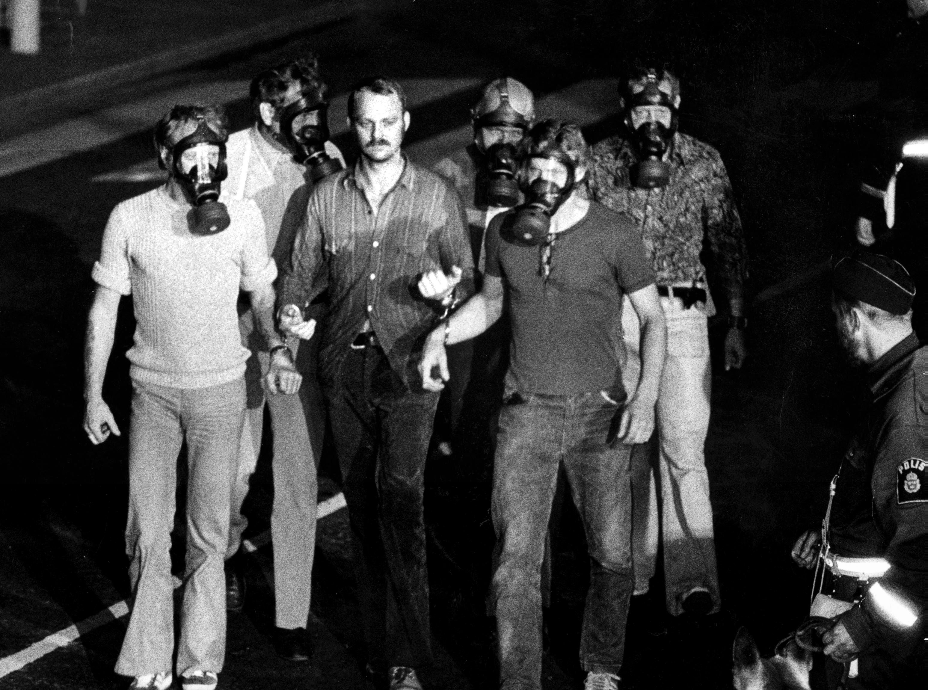 Police officers, with gas masks, take Jan-Erik Olsson away in handcuffs on 28 August 1973, after a standoff that lasted more than five days