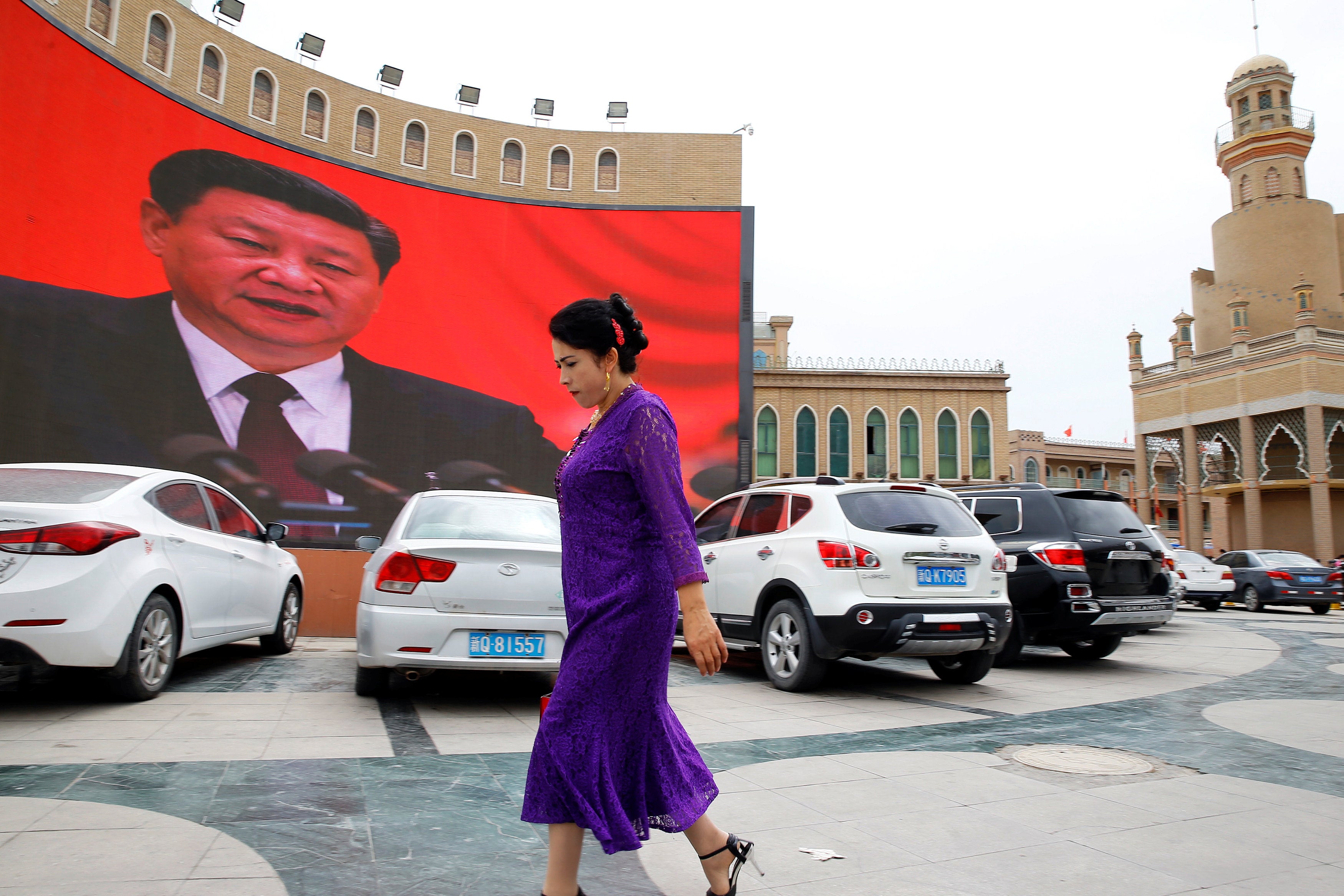 An ethnic Uighur woman walks in front of a giant screen with a picture of Chinese president Xi Jinping