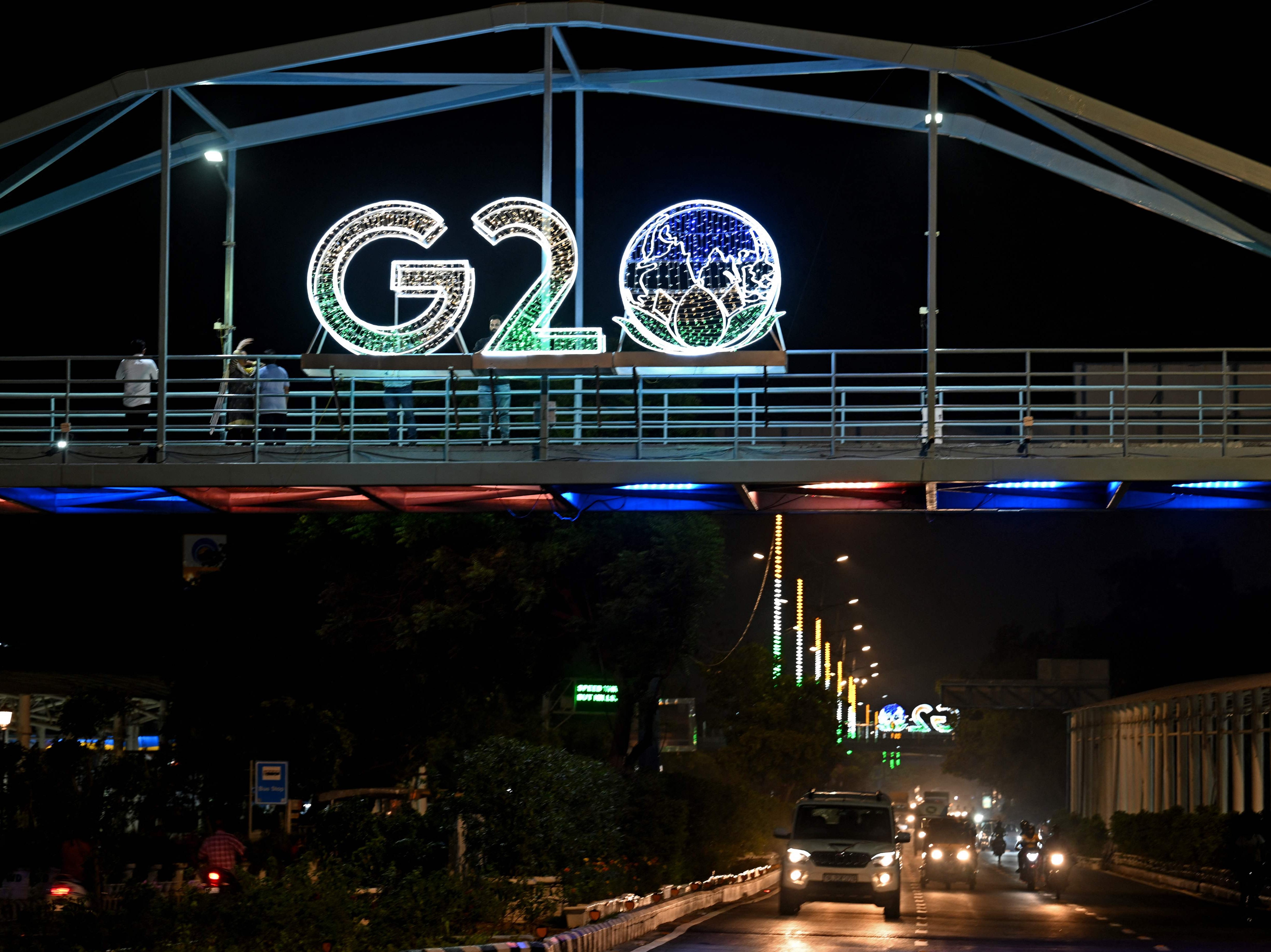 Vehicles ride under an illuminated hoarding with the G20 logo displayed over a bridge in New Delhi