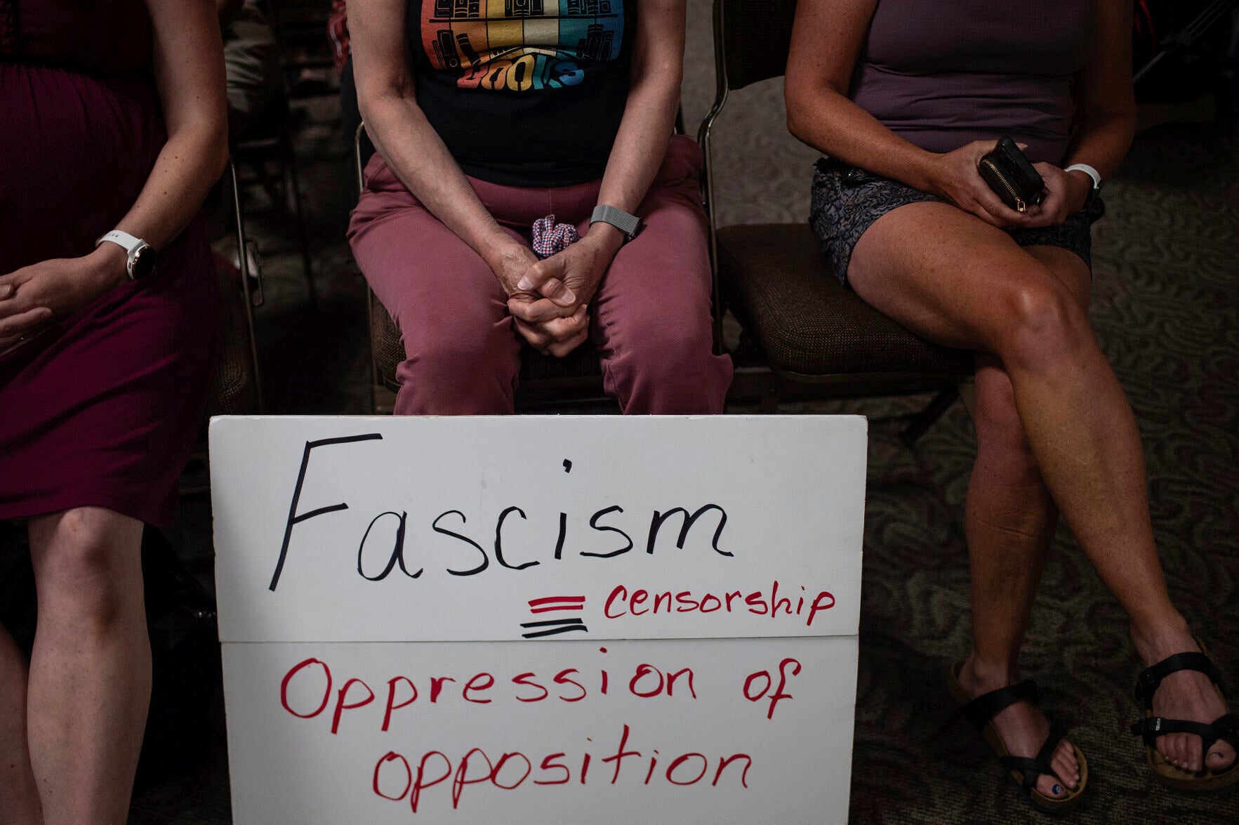 Three people sit with a sign at a Campbell County, Wyoming, Library Board meeting in 2023