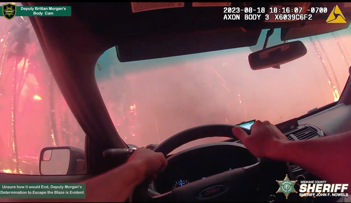 Flames lick the side of a Spokane County Sheriff’s deputy as he races through a wildfire on 18 August