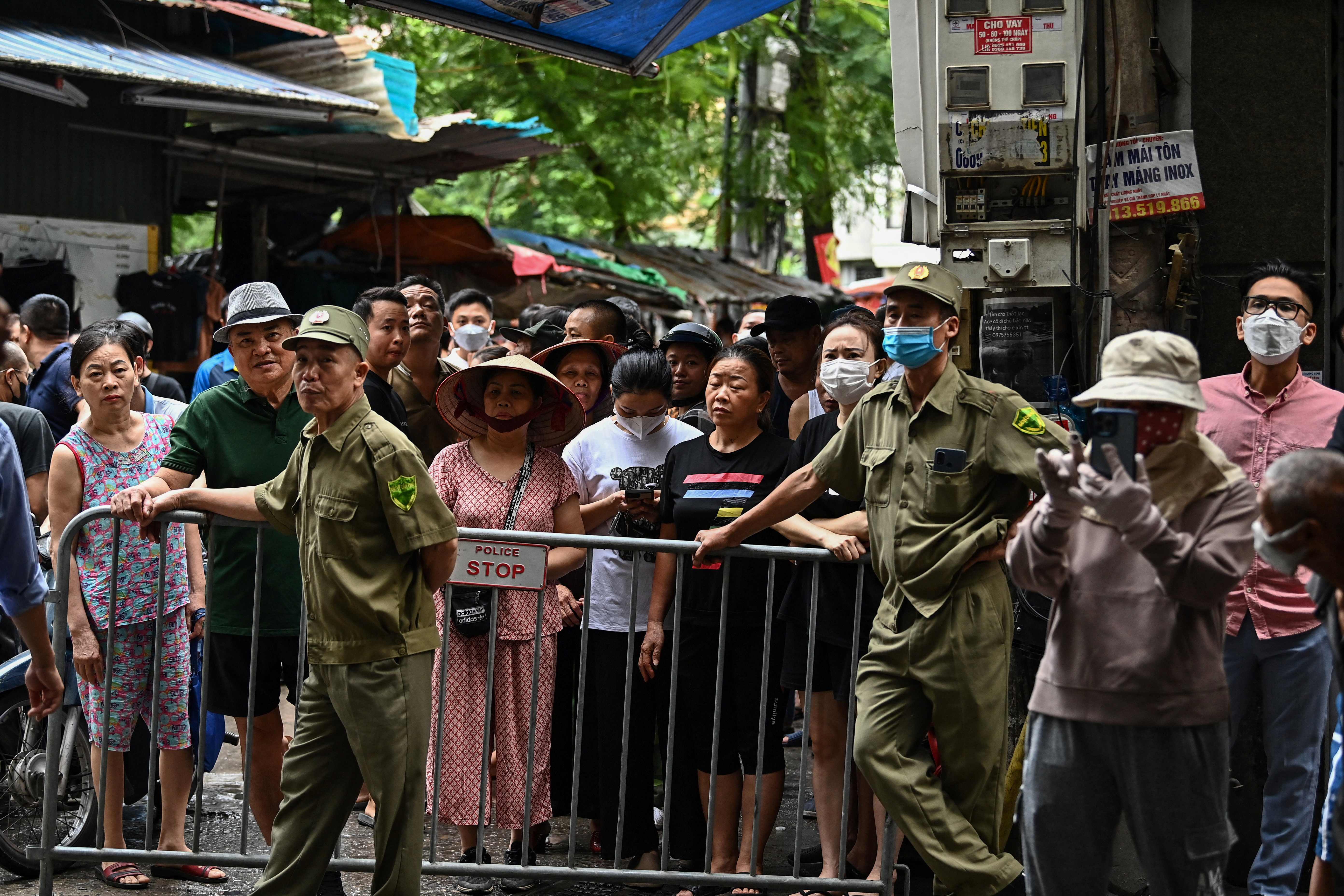 Residents stand behind a barrier near the site of a major fire at an apartment block in Hanoi