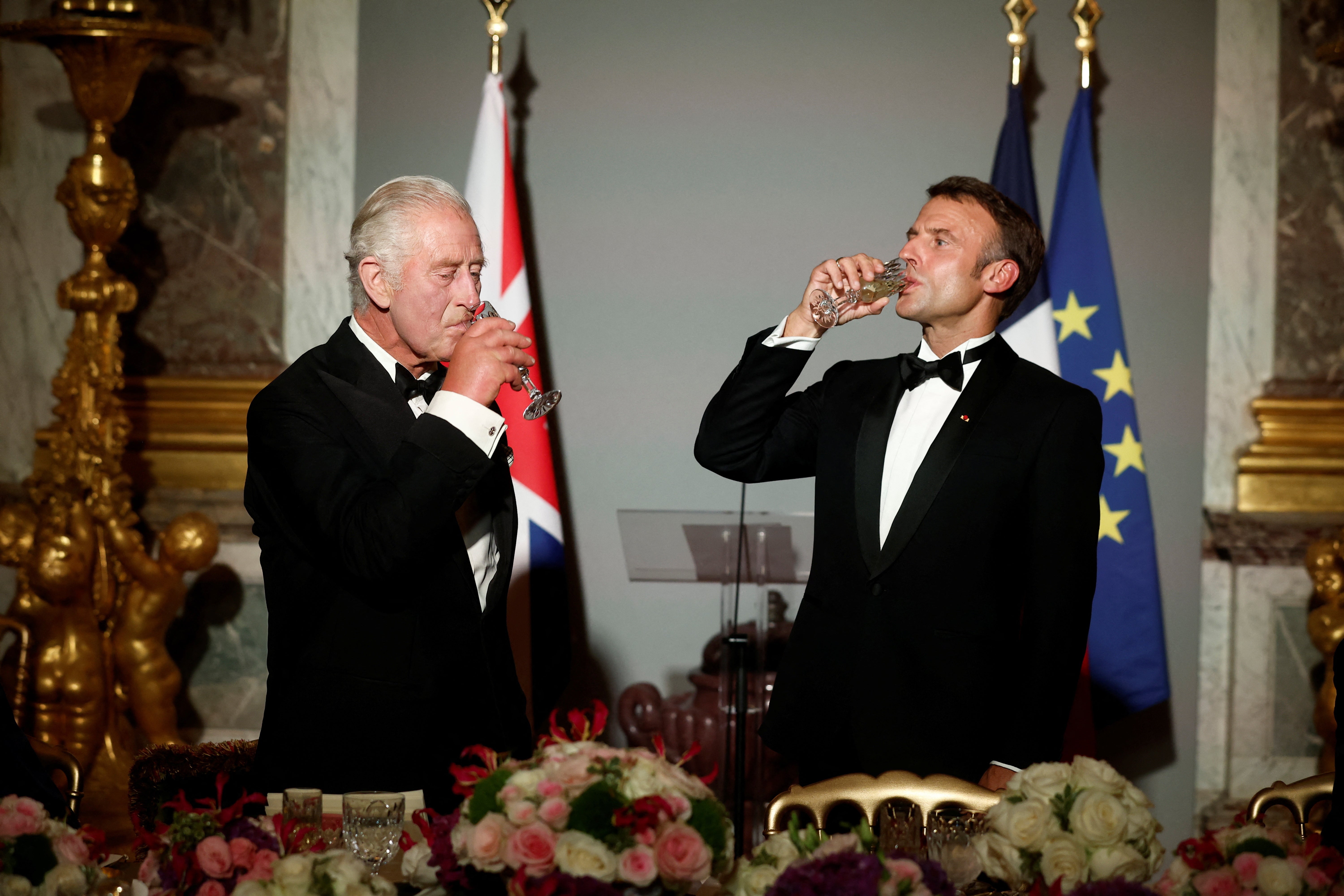 French President Emmanuel Macron (right) and Britain's King Charles III drink after toasting during a state dinner in the Hall of Mirrors at the Palace of Versailles