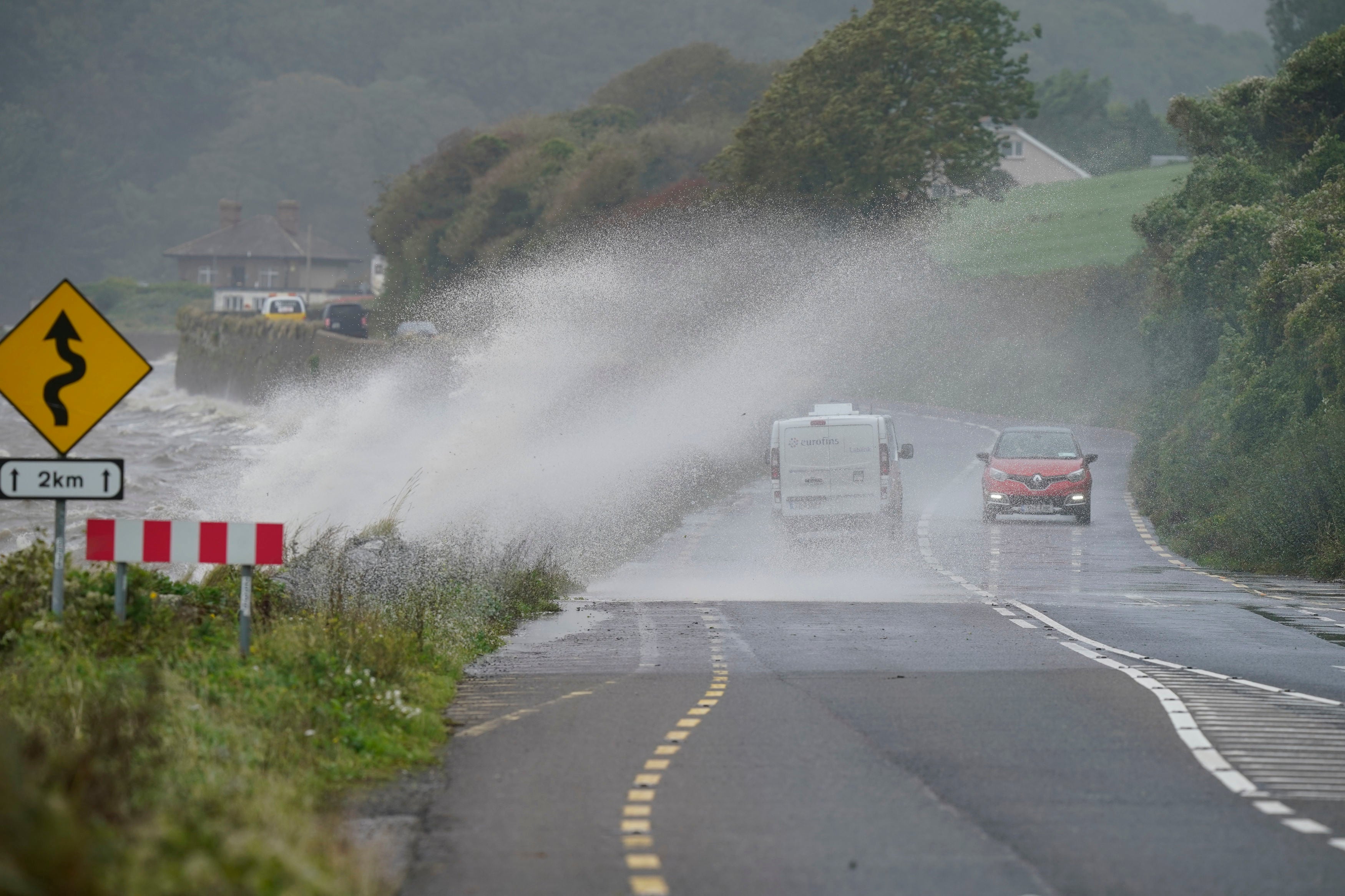 Cars pass waves crashing over a wall into the road in Youghal, Co Cork