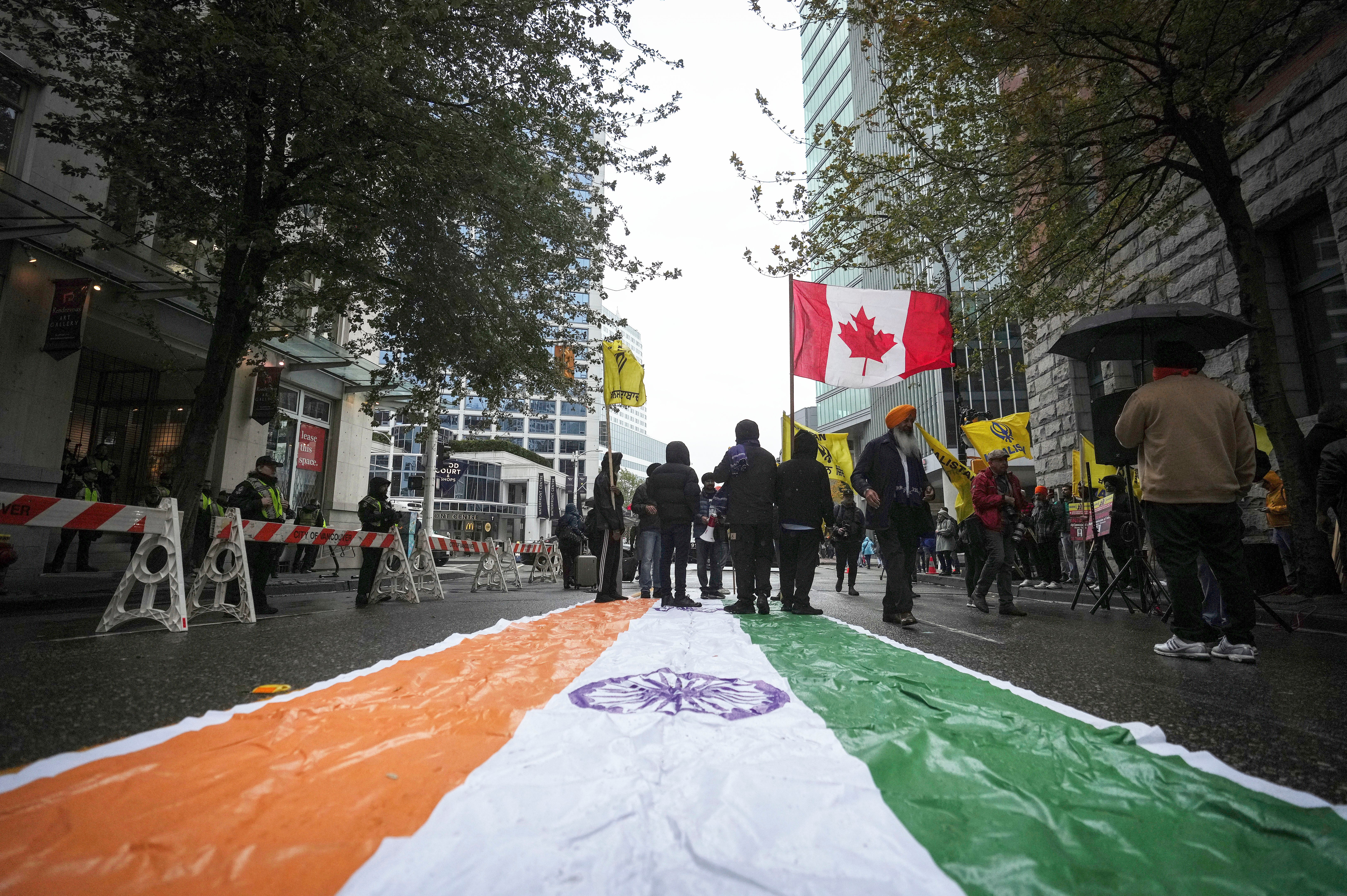 An Indian flag is laid on the street as protesters wave a Canadian and Khalistan flags during a protest outside the Indian Consulate in Vancouver