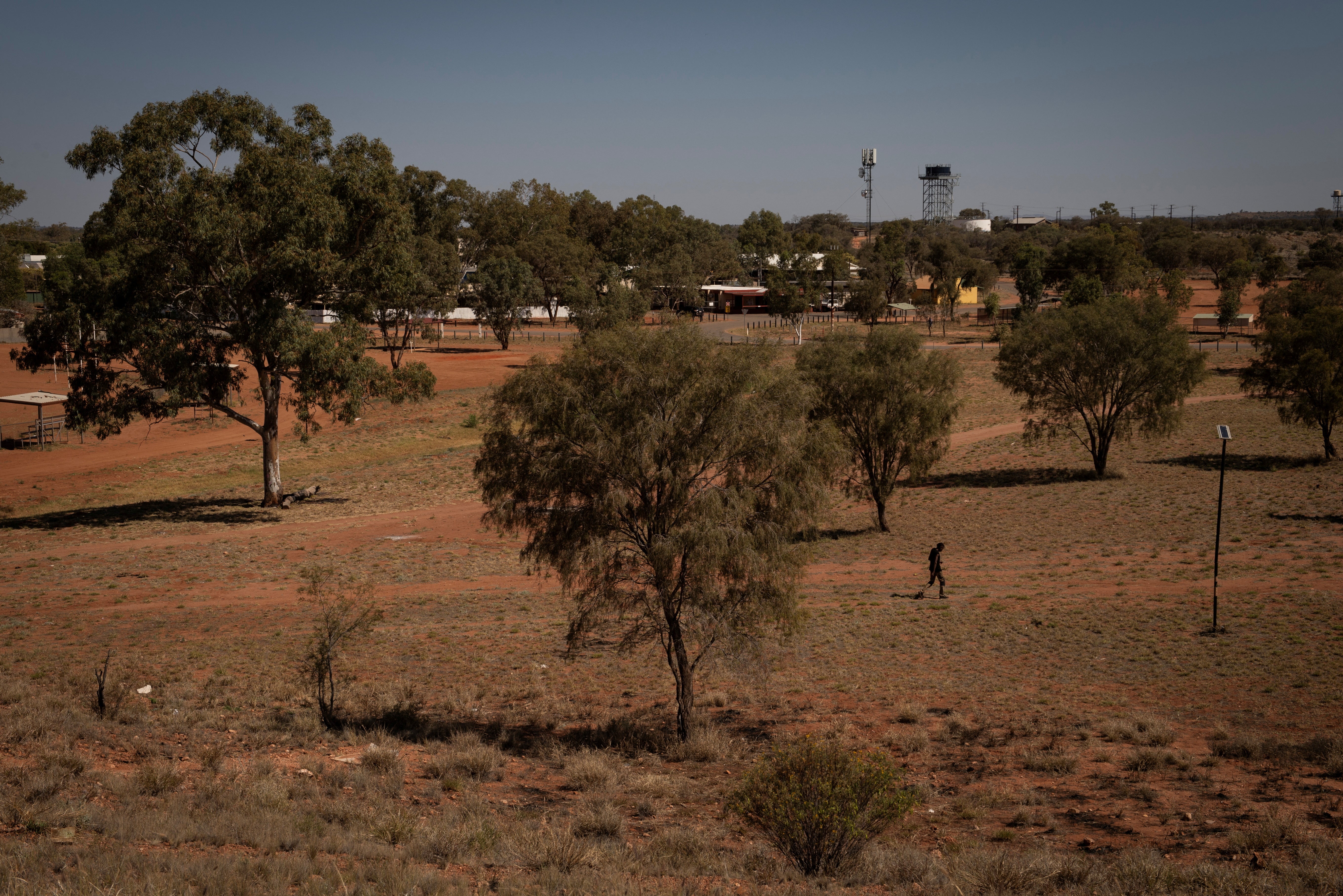 A man walks across a park towards town in Hermannsburg, near Areyonga