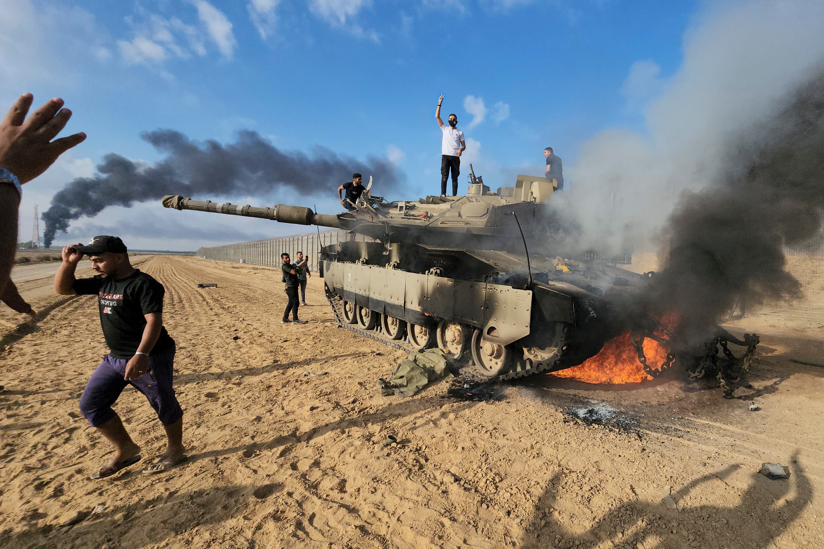 Hamas militants next to a destroyed Israeli tank at the Gaza Strip fence east of Khan Younis