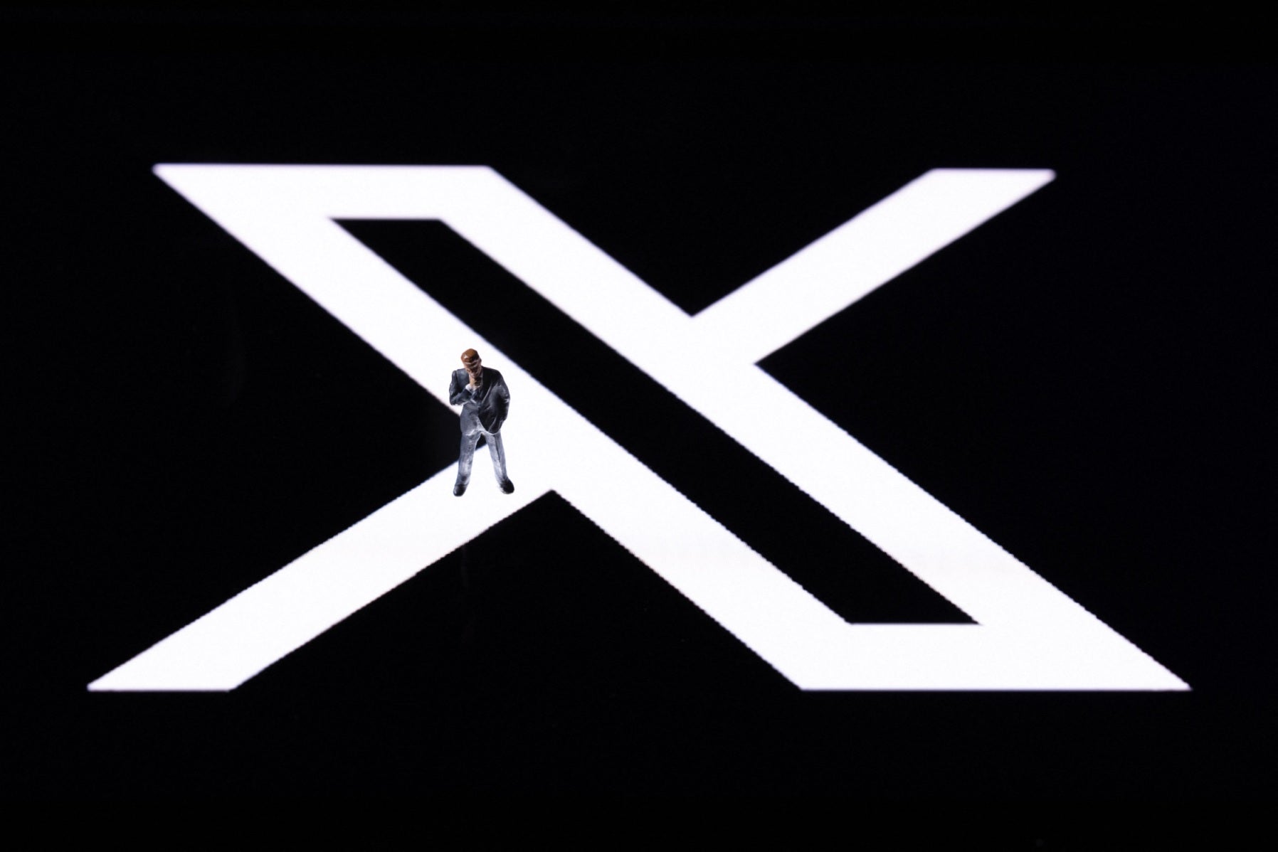 This illustration photo shows a figurine displayed on the new Twitter logo rebranded as X reflected in smartphone screen, in Paris on 27 July, 2023