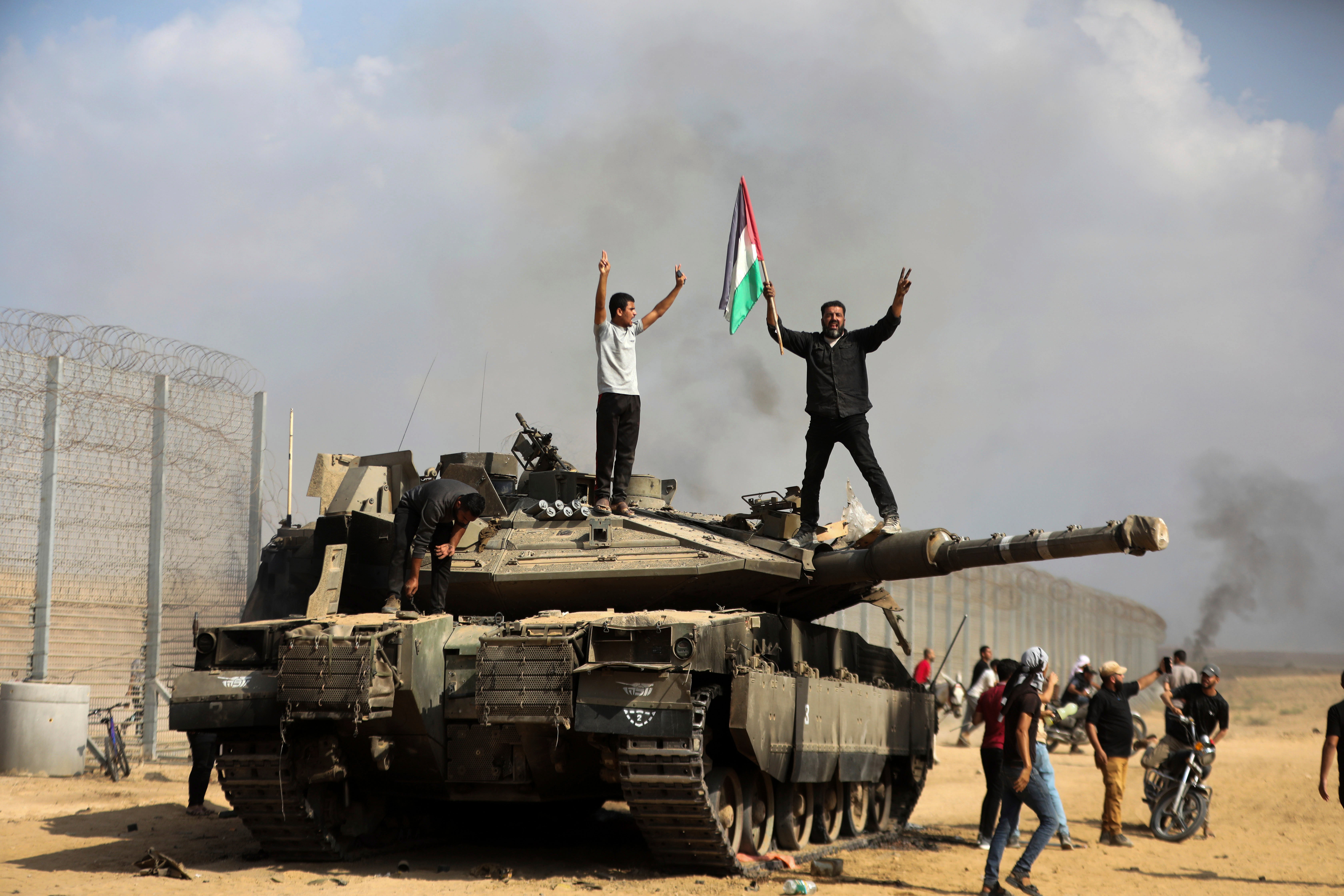 Palestinians wave their national flag and celebrate by a destroyed Israeli tank at the Gaza Strip fence east of Khan Younis southern Saturday, Oct. 7, 2023.